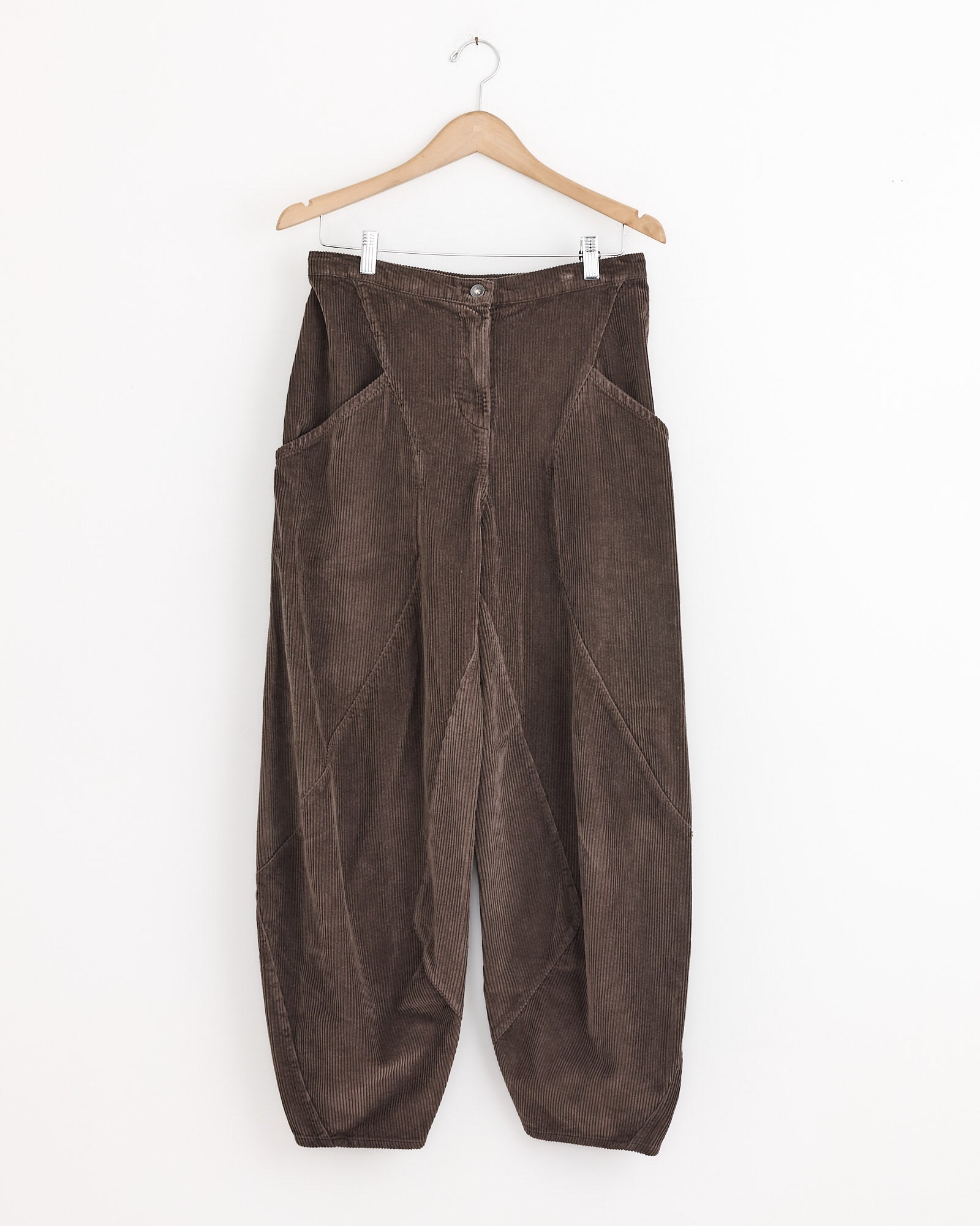 Henrik Vibskov Digi Corduroy Pant in Chocolate Brown features wide legs, large side pockets, and a button-zipper closure, displayed on a wooden hanger against a plain white background.