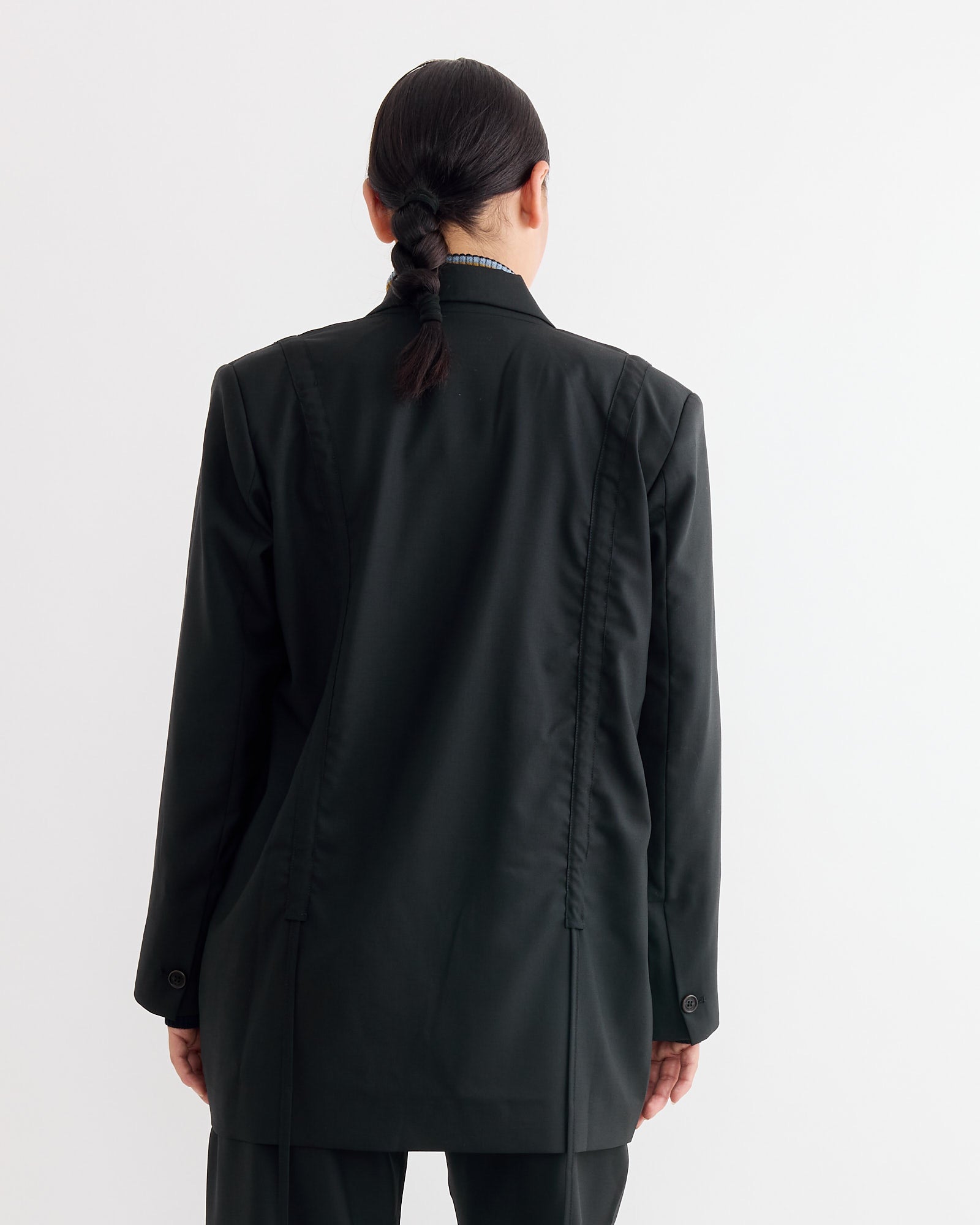 A person with dark braided hair is seen from behind wearing the Henrik Vibskov Backpack Blazer in Tropical Black, standing against a plain white background.