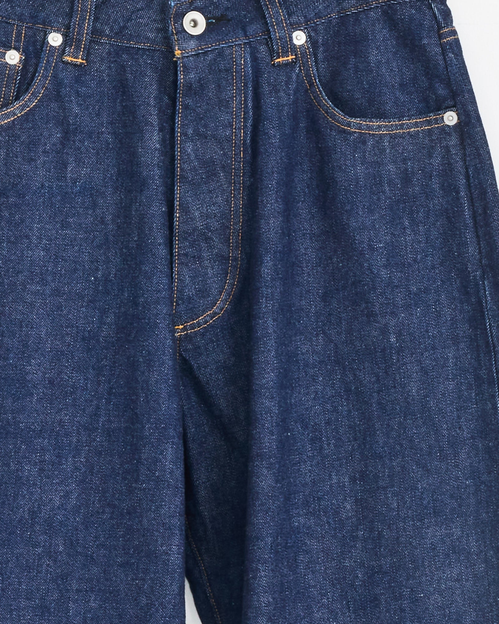 Close-up of the Seb Jean in Indigo Wash by Studio Nicholson, showing the front pockets, button, and signature orange stitching on Japanese denim.