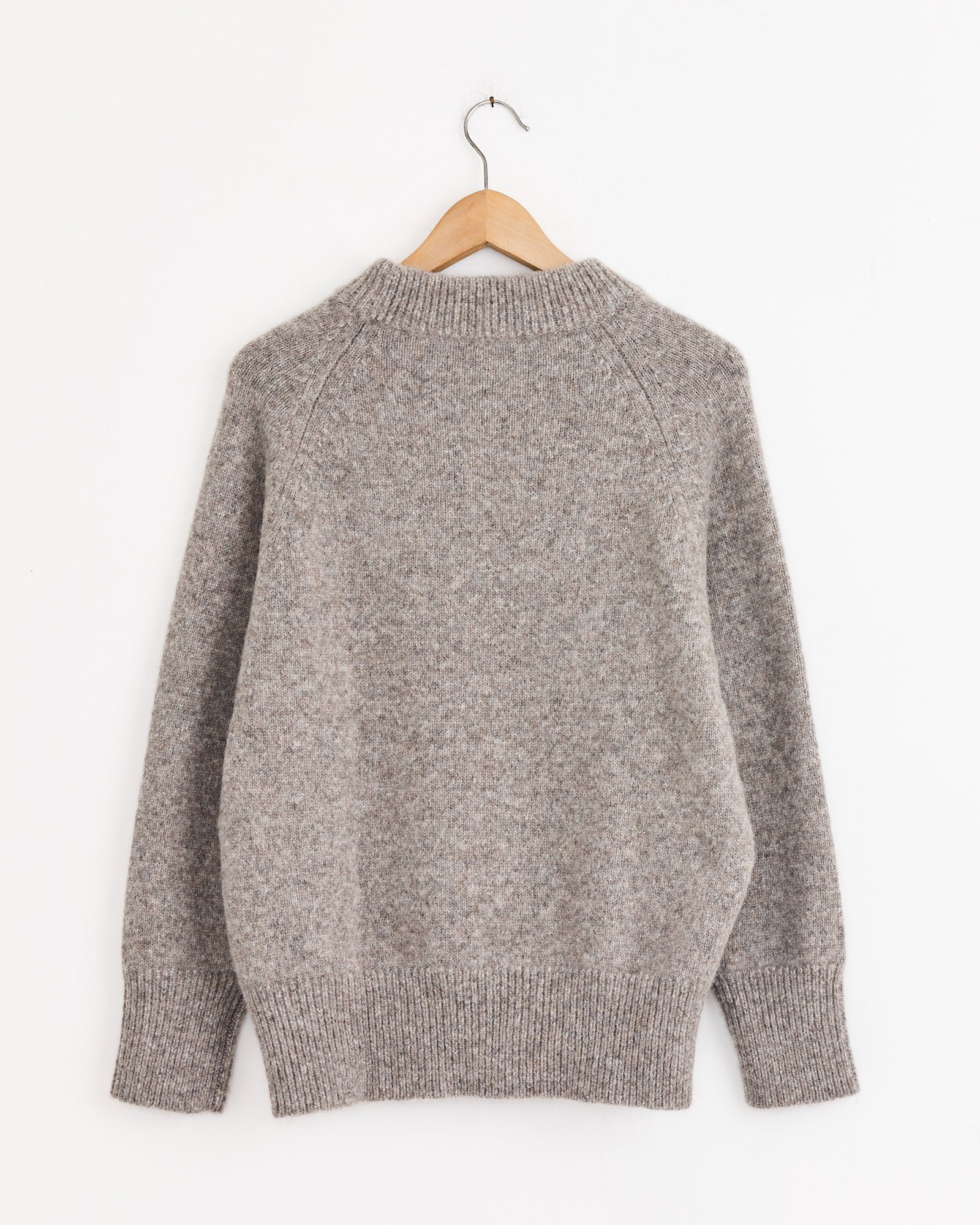 A Studio Nicholson Persephone Crewneck in Natural, featuring long sleeves and ribbed cuffs and hem, is displayed on a wooden hanger against a plain white background.