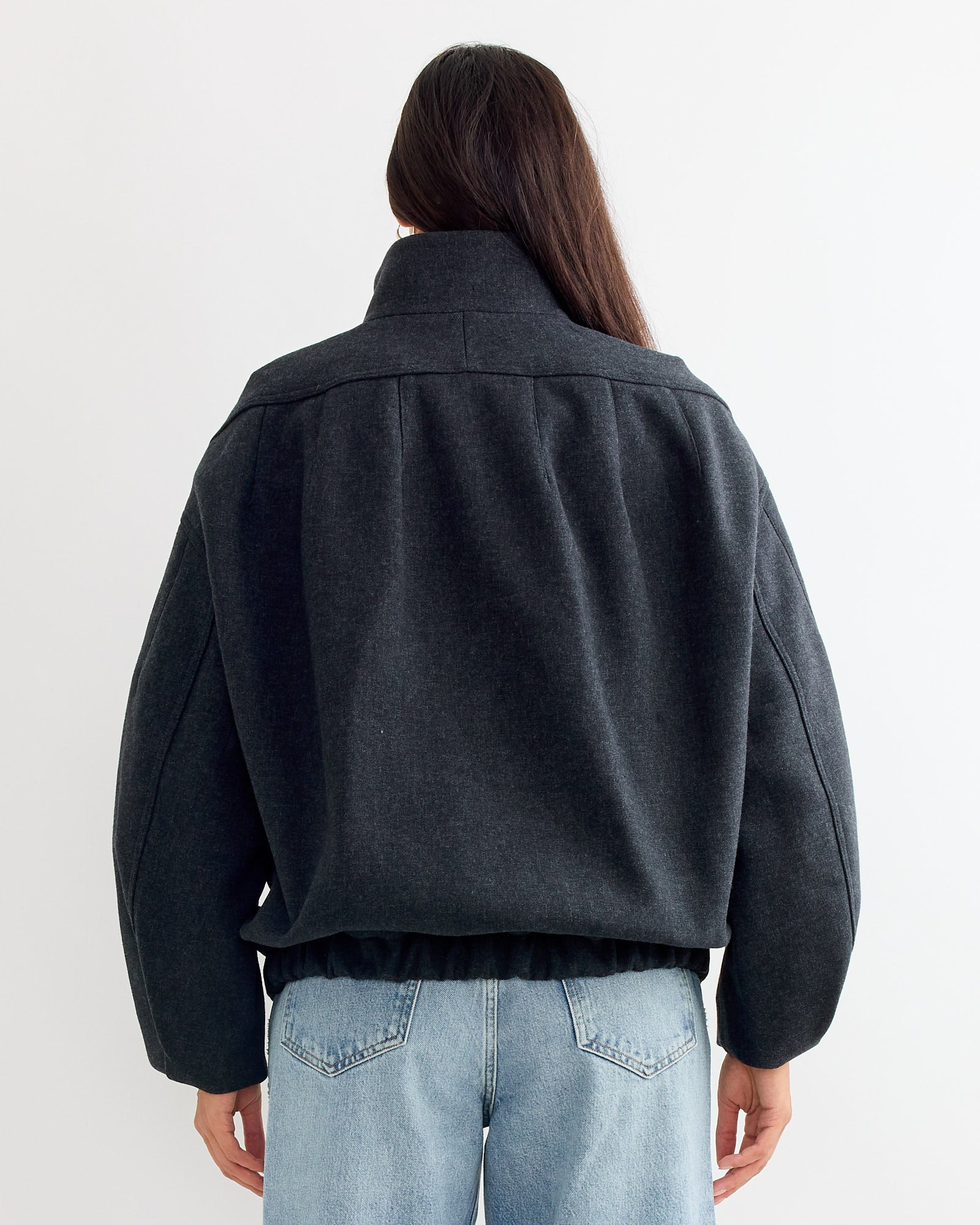 A person with long dark hair, wearing the Dries Van Noten Loose Fit Jacket in Dark Grey and light blue jeans, stands with their back to the camera against a plain light background.