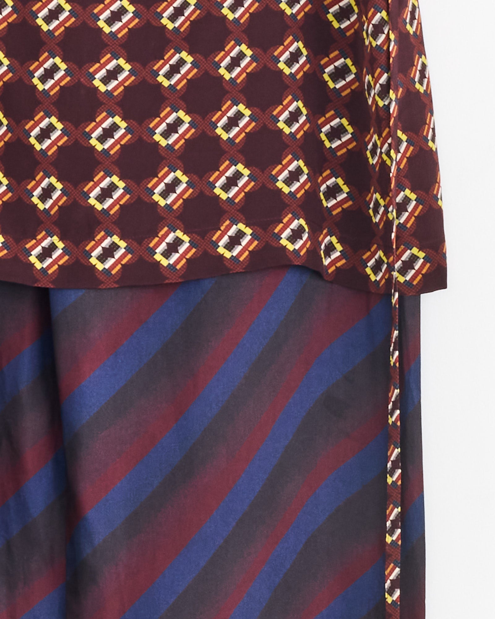 A close-up of Dries Van Noten Printed Skirt Pants in Navy, featuring diagonal maroon and navy blue stripes, paired with a geometric patterned maroon top.