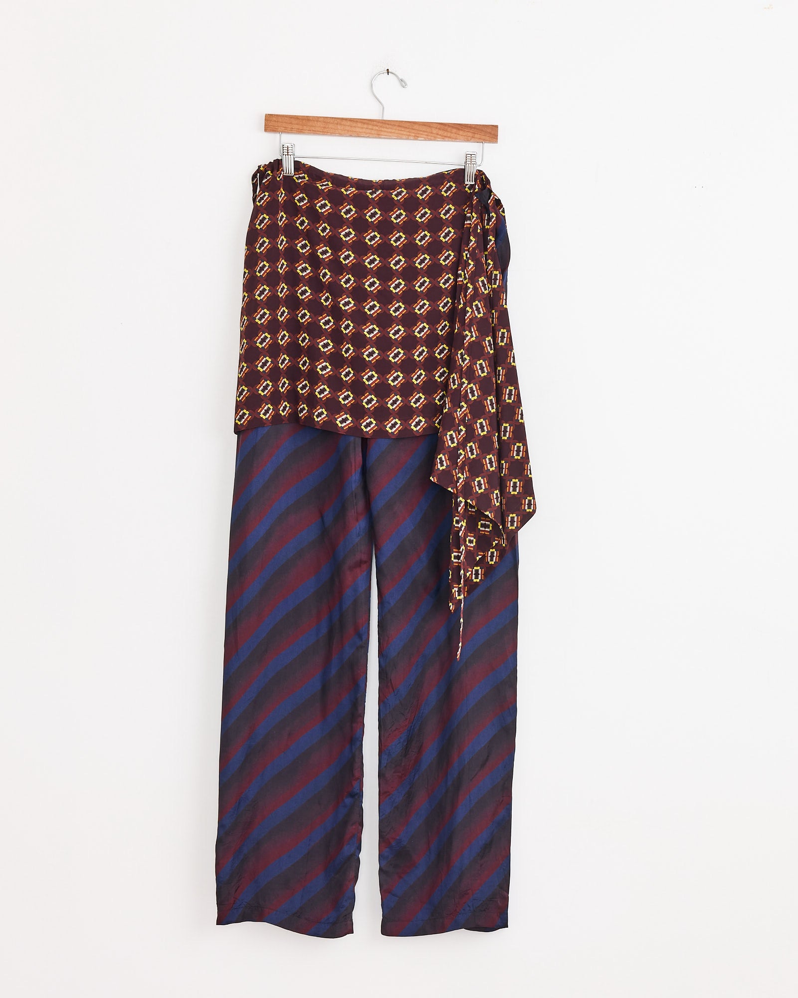 Printed Skirt Pants in Navy by Dries Van Noten feature loose, wide legs with diagonal navy and maroon stripes, complemented by a brown and yellow geometric print skirt wrap, shown on a hanger against a white background.