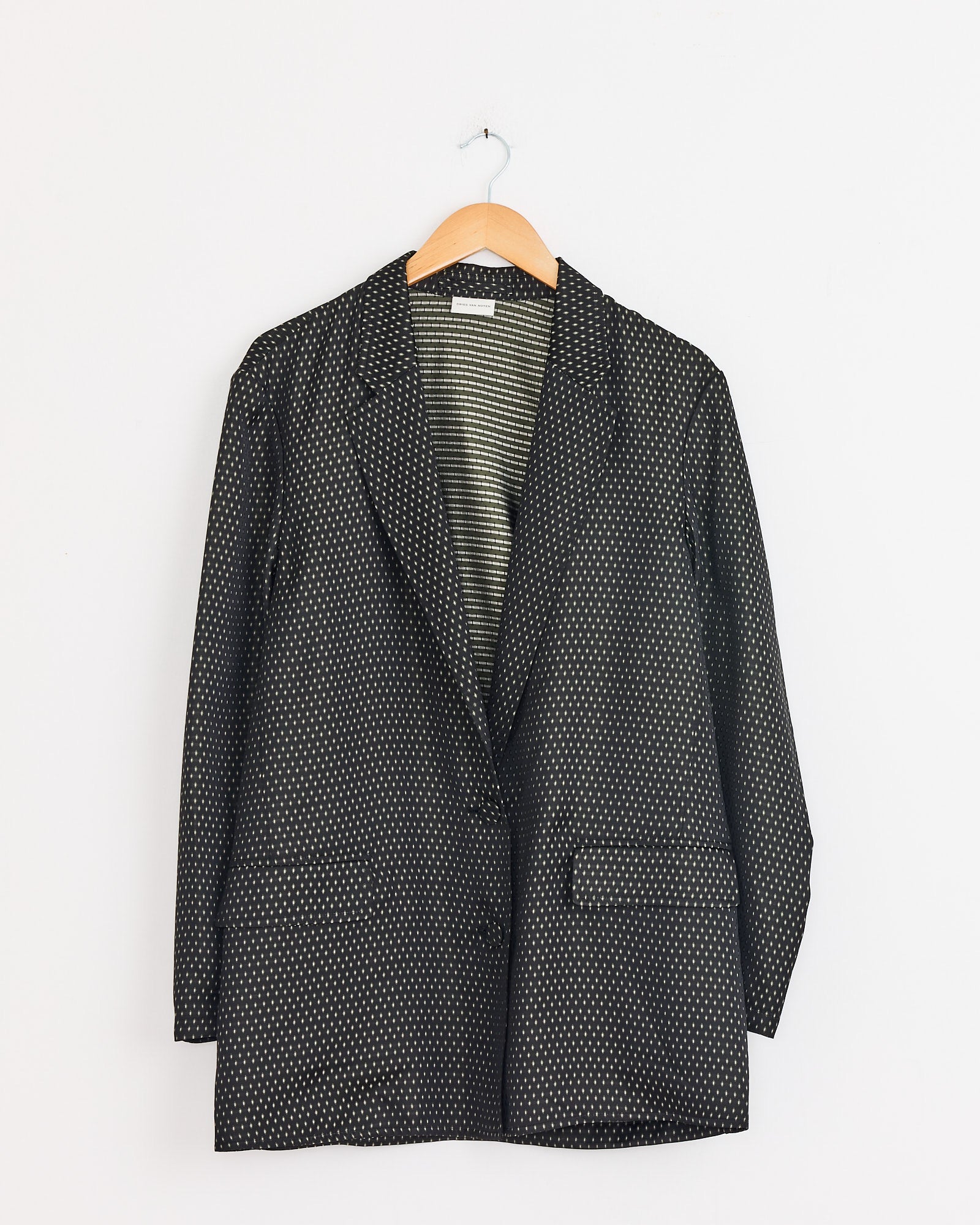 The Dries Van Noten Jacquard Double-Breasted Blazer in black, featuring a subtle white dotted pattern, is displayed on a wooden hanger against a plain white background.
