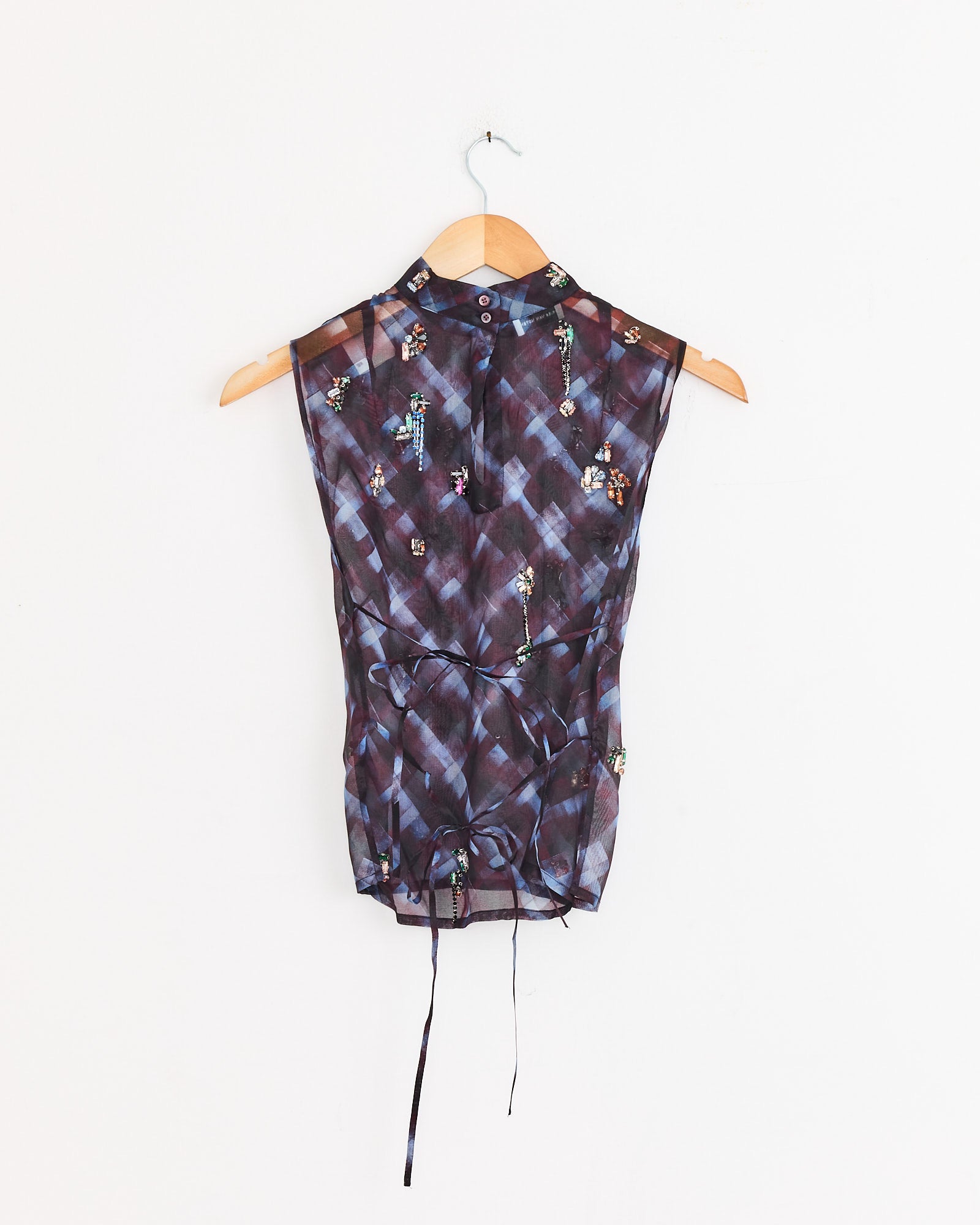 The Dries Van Noten Embellished Top in Burgundy, a sleeveless, semi-sheer blouse with floral embroidery and a high collar, hangs on a wooden hanger against a plain white wall.