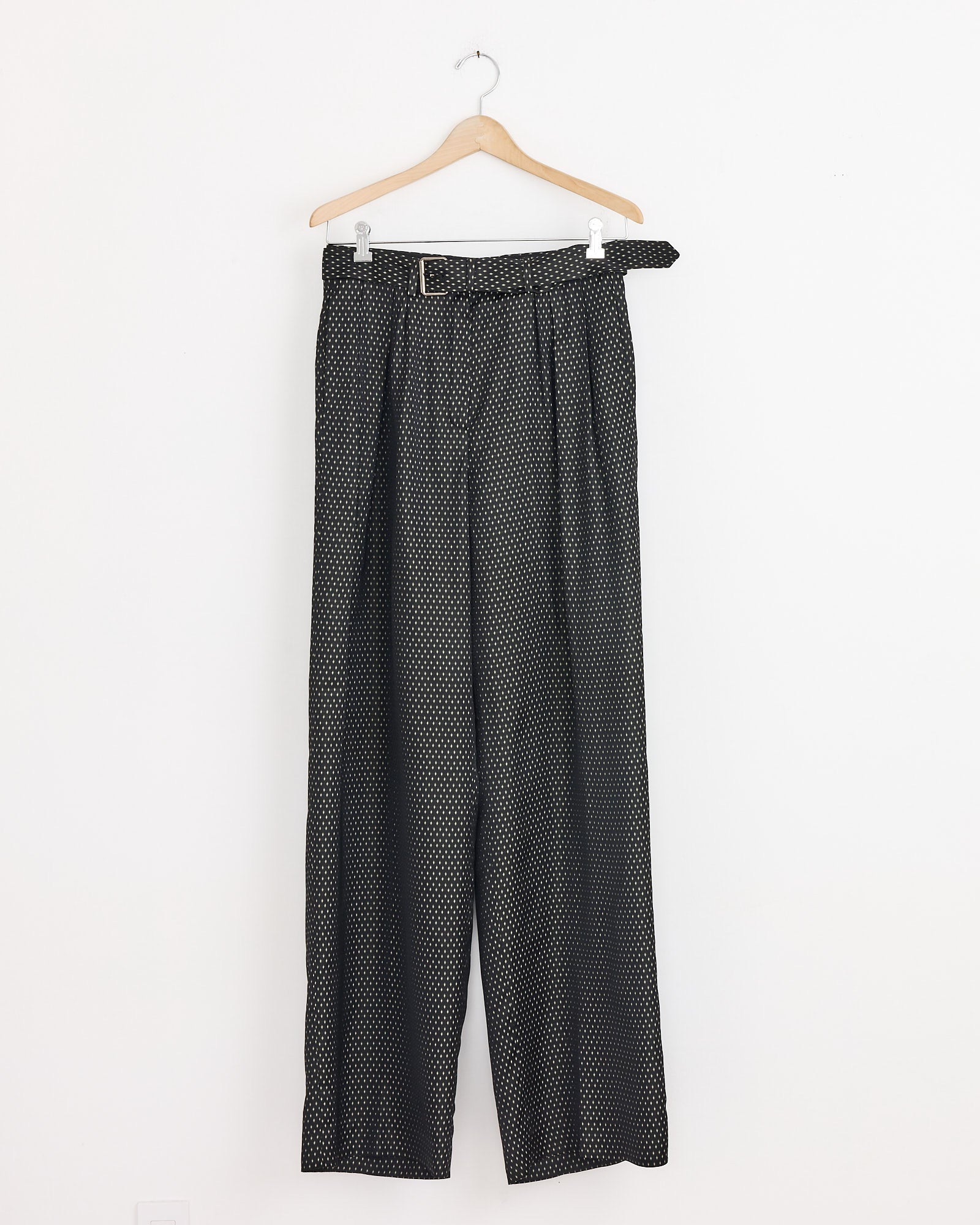 Dries Van Noten Belted Jacquard Trousers in Black, featuring a white polka dot pattern, wide legs, high waist with pleats and matching belt, displayed on a wooden hanger against a plain white wall.
