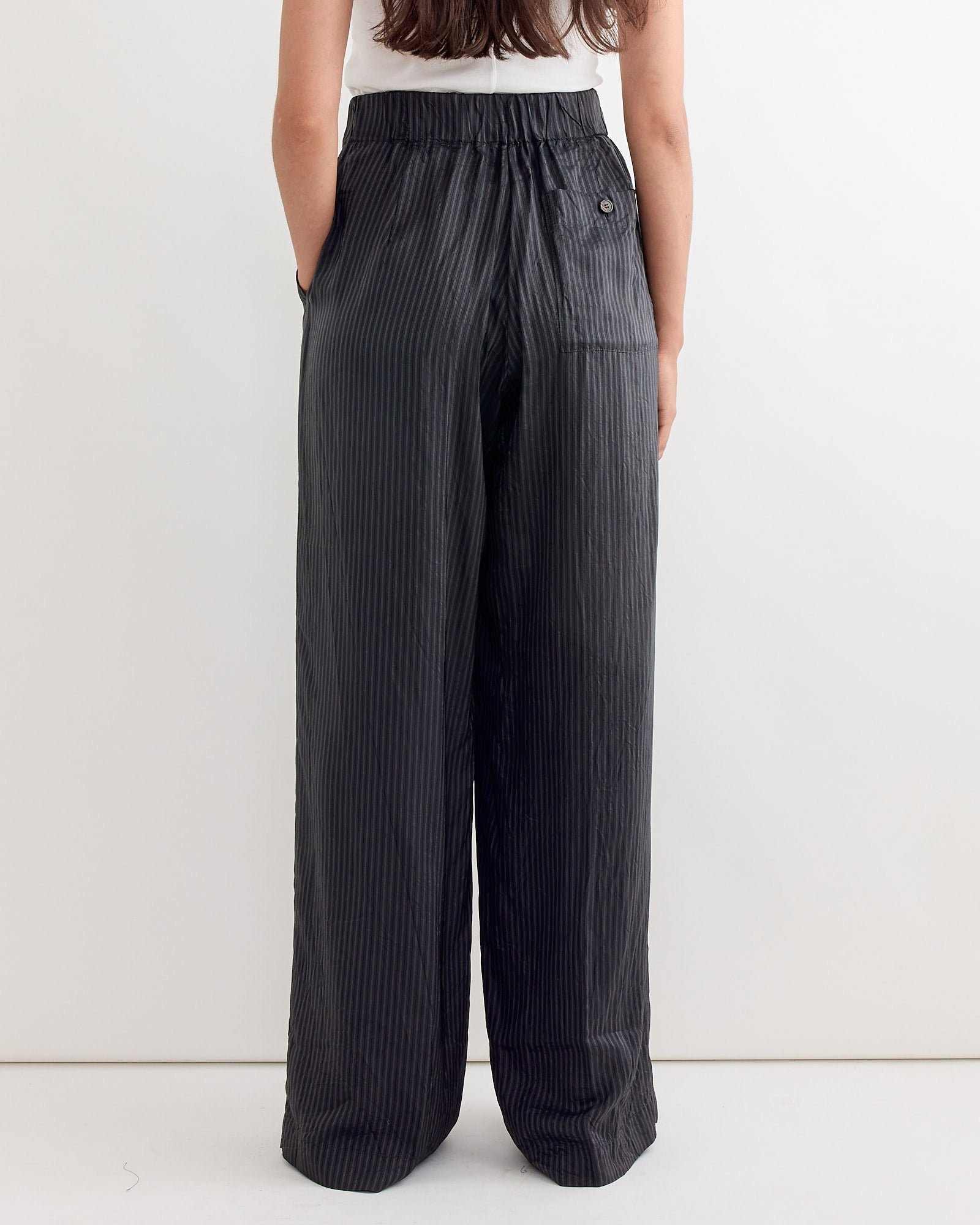 A woman with long brown hair, seen from behind, wears a white sleeveless top and Dries Van Noten's Wide Leg Striped Pant in Grey with an elastic waistband and side pockets, showcasing a voluminous silhouette against a plain white background.