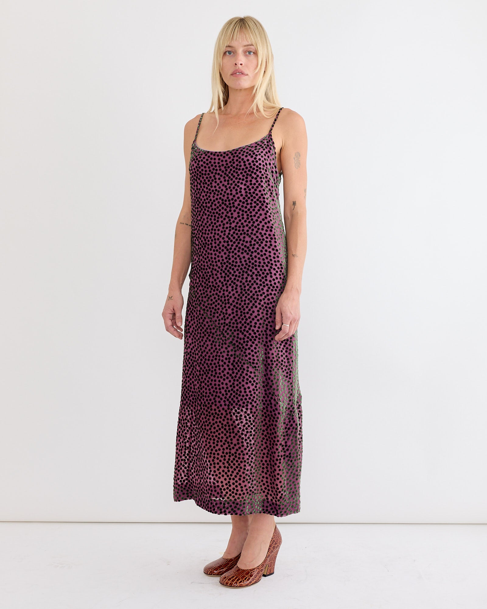 A person with blonde hair wears a sleeveless, ankle-length Dries Van Noten Slip Dress in Dark Pink and brown heels, standing against a plain white background.