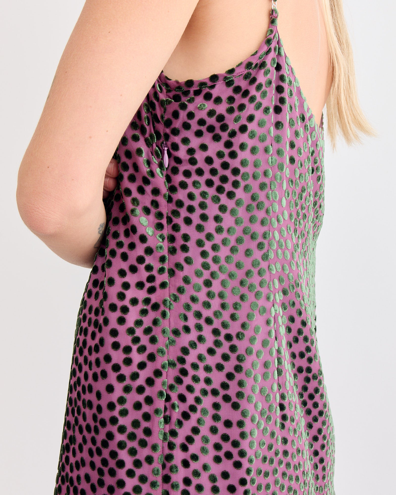 A close-up shows a person wearing a sleeveless Dries Van Noten Slip Dress in Dark Pink, viewed from the side and back with arms crossed and partially visible long blond hair.