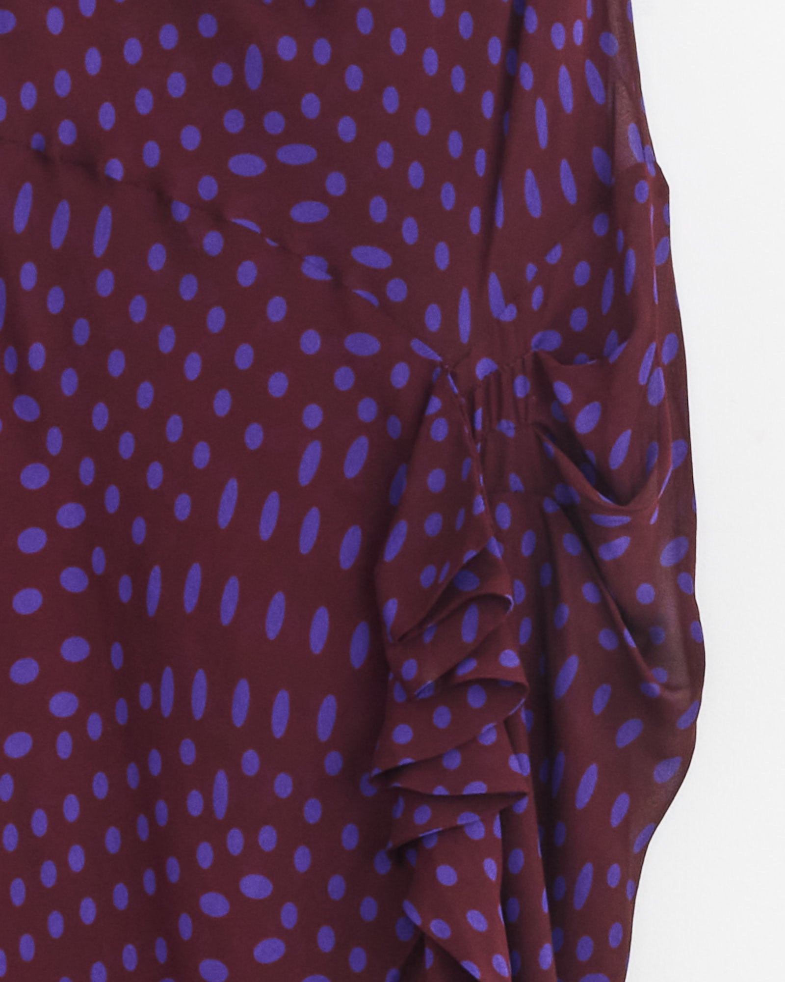 Close-up of the Dries Van Noten Asymmetric Dress in Auber, featuring maroon viscose georgette with blue polka dots and an angled layered ruffle on the right side.