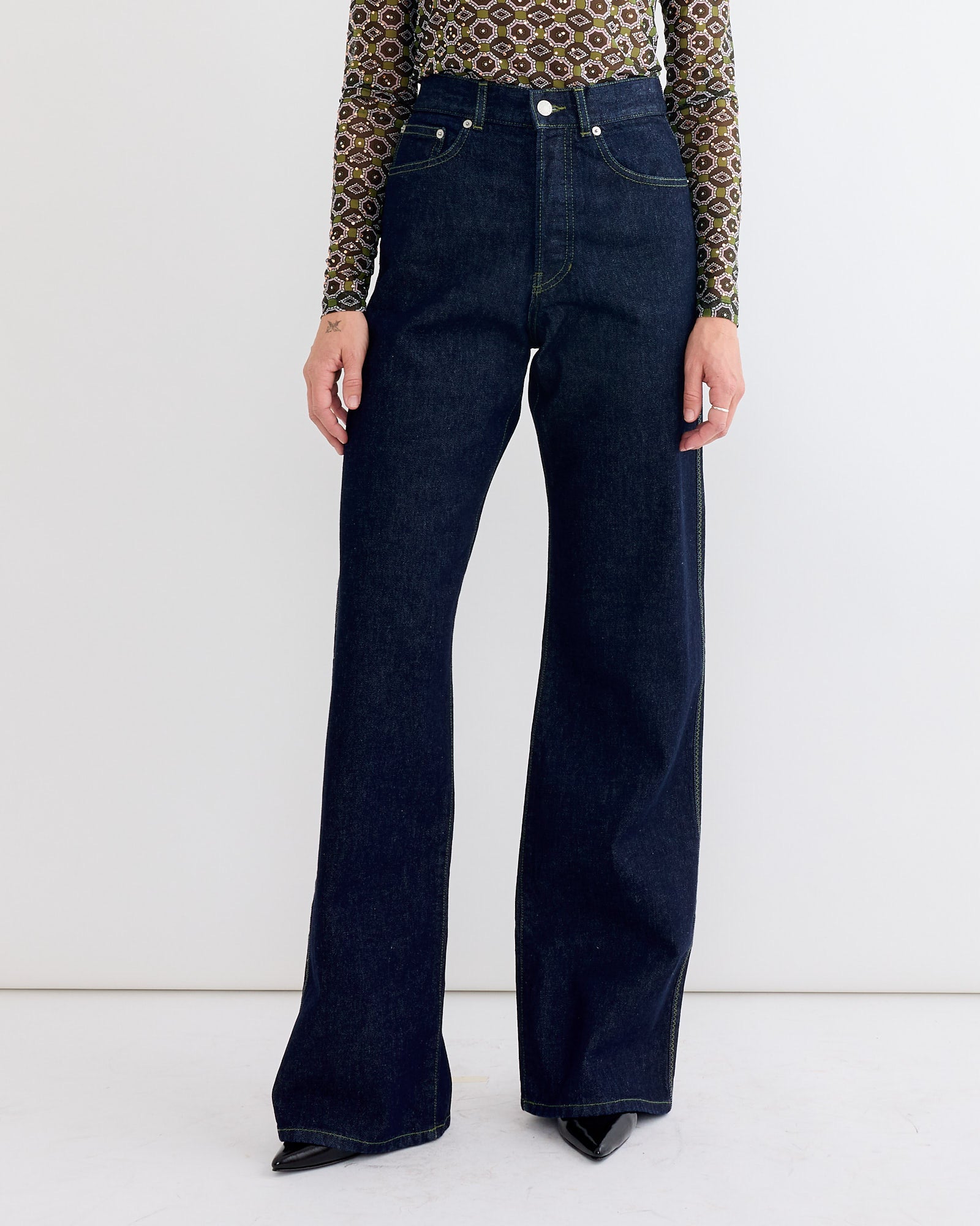 A person stands against a white background wearing Dries Van Noten Wide-leg Pants in Indigo, a patterned long-sleeve top, and pointed black shoes.
