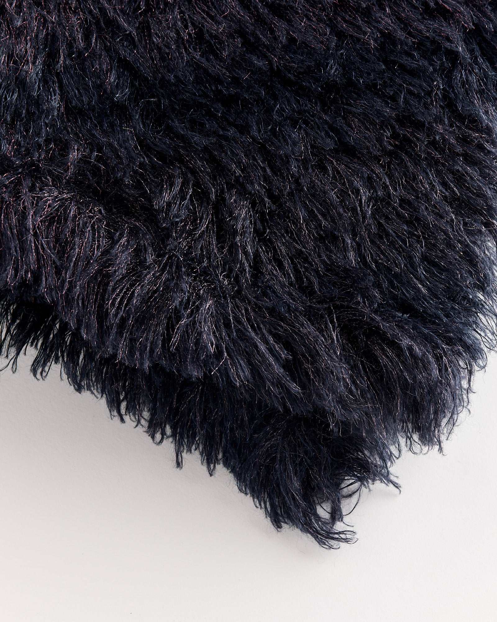 Close-up of the Tejar 2732 Scarf in Purple by Dries Van Noten, featuring dark, shaggy, long fibers with a soft, dense texture. Shown on a smooth, light grey surface—contact our online chat for fit and sizing advice.