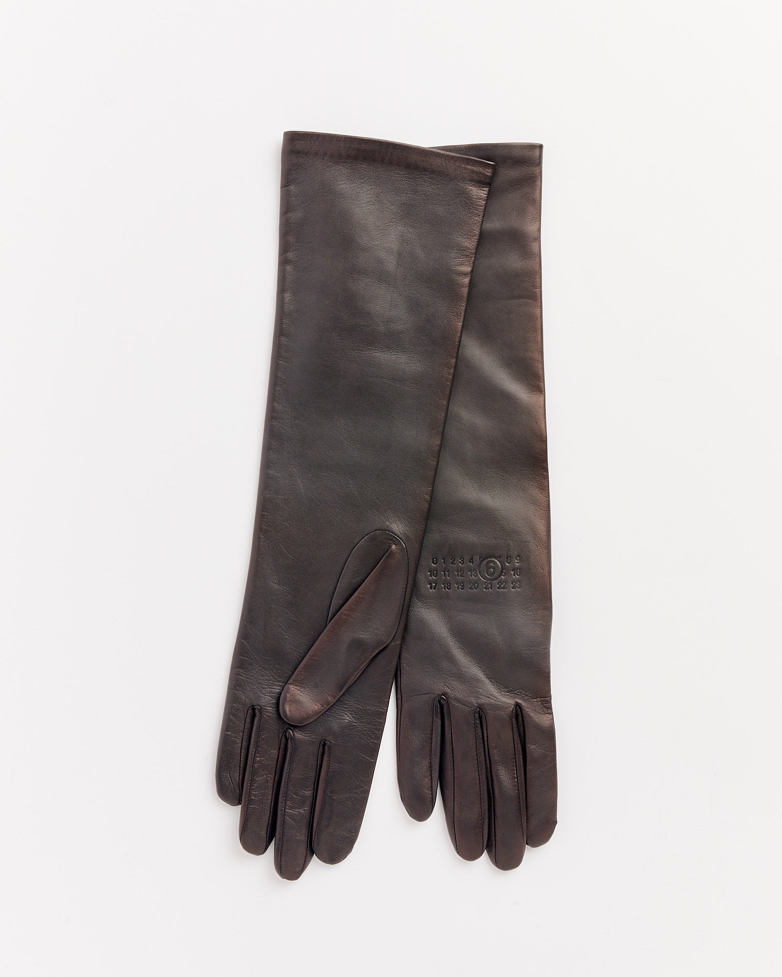 A pair of long black MM6 Maison Margiela leather gloves with subtle embossed text on the wrist are laid flat on a white background; contact our online chat for sizing and fit advice.