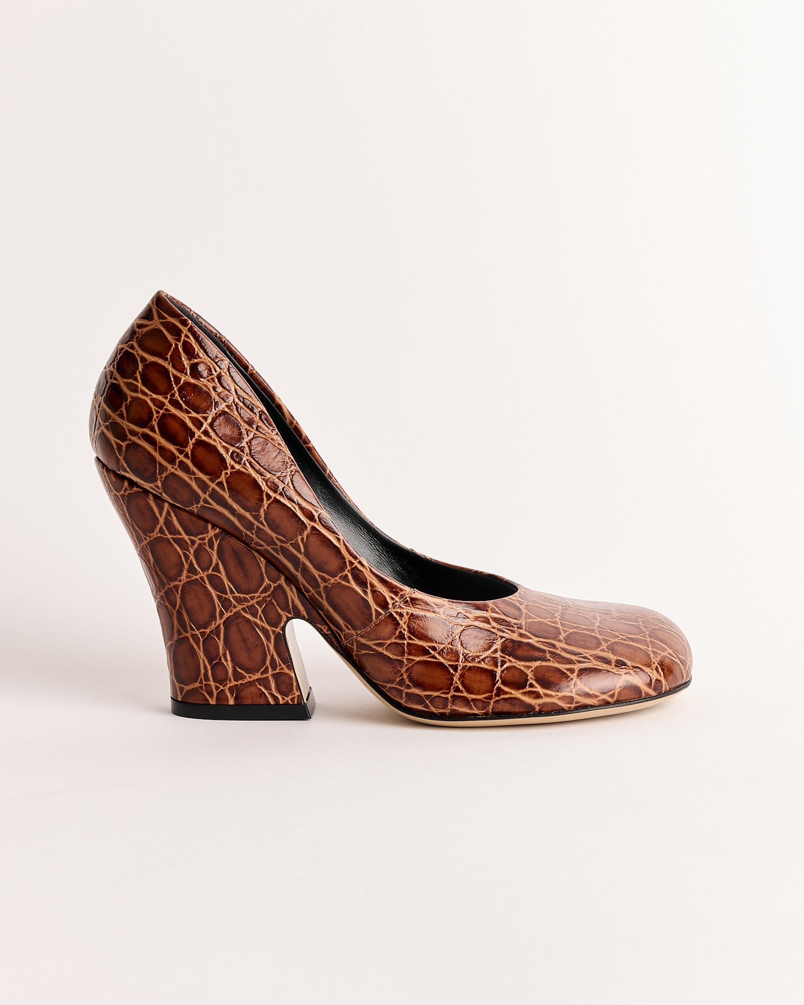 The “Embossed Heel in Tan” by Dries Van Noten features textured faux crocodile leather, a rounded toe, and a high heel, shown against a plain light background.