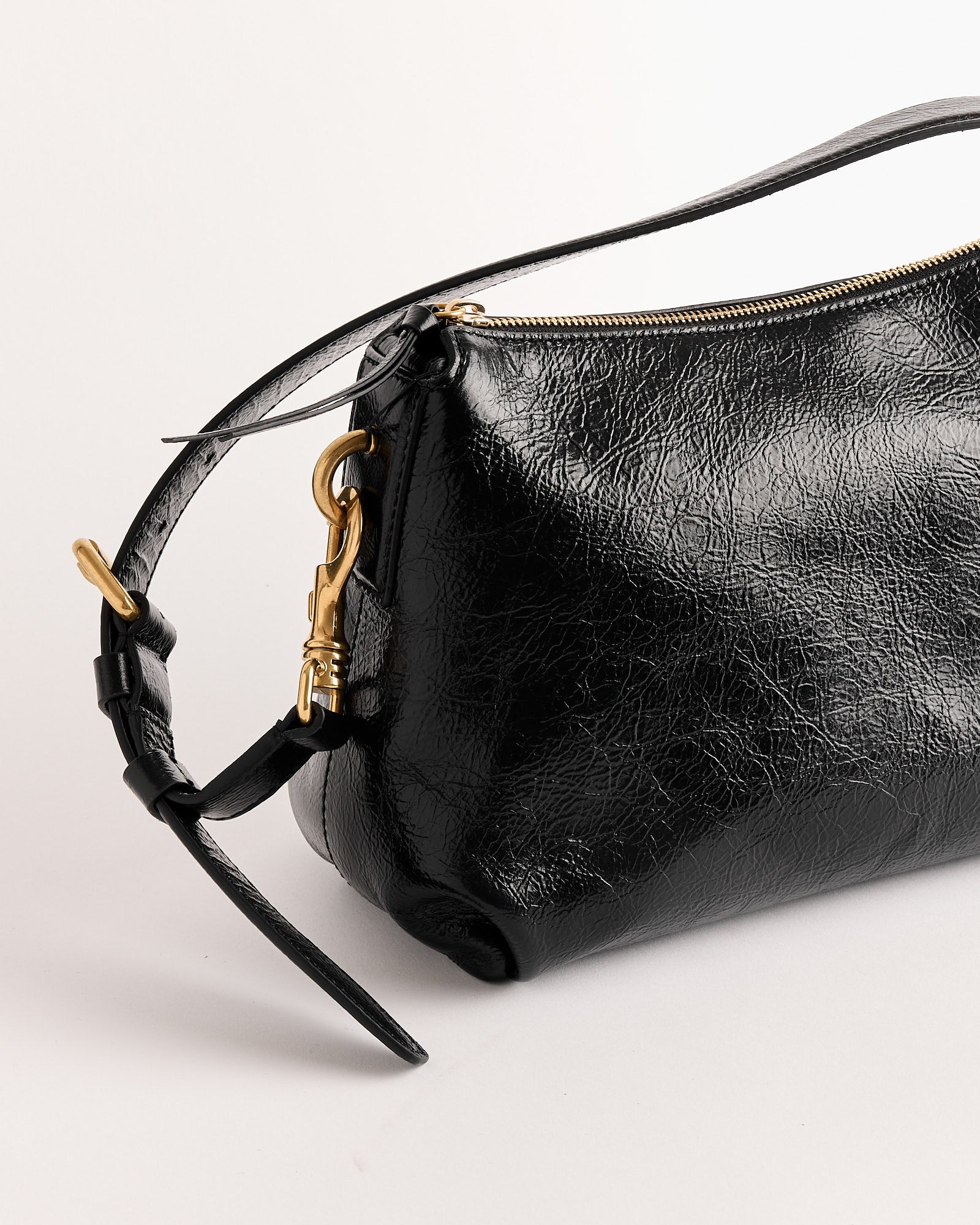 A close-up of the Dries Van Noten Grip Bag in glossy black leather, featuring a gold zipper and hardware on the strap, photographed against a plain light background. Expertly crafted in Italy.