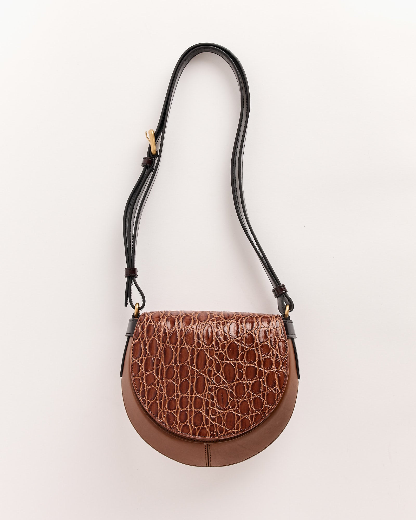 The Dries Van Noten Arc Bag is a tan crossbody featuring a croc-embossed leather flap, smooth lower section, gold hardware, and a long adjustable black strap, shown against a light background.