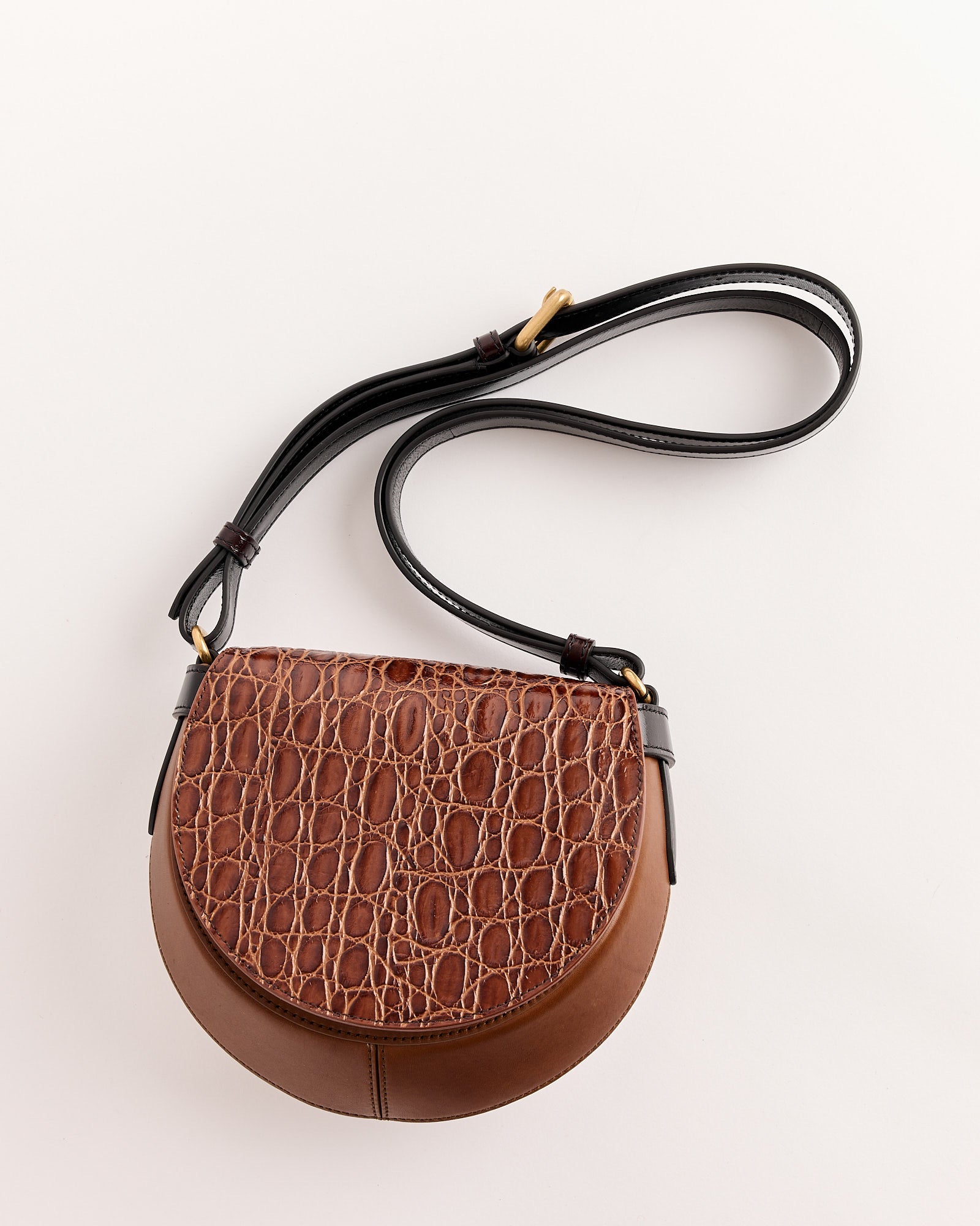 The Dries Van Noten Arc Bag is a tan croc-embossed leather crossbody with a textured flap, smooth leather base, long black adjustable strap, and gold-tone hardware shown against a light background.