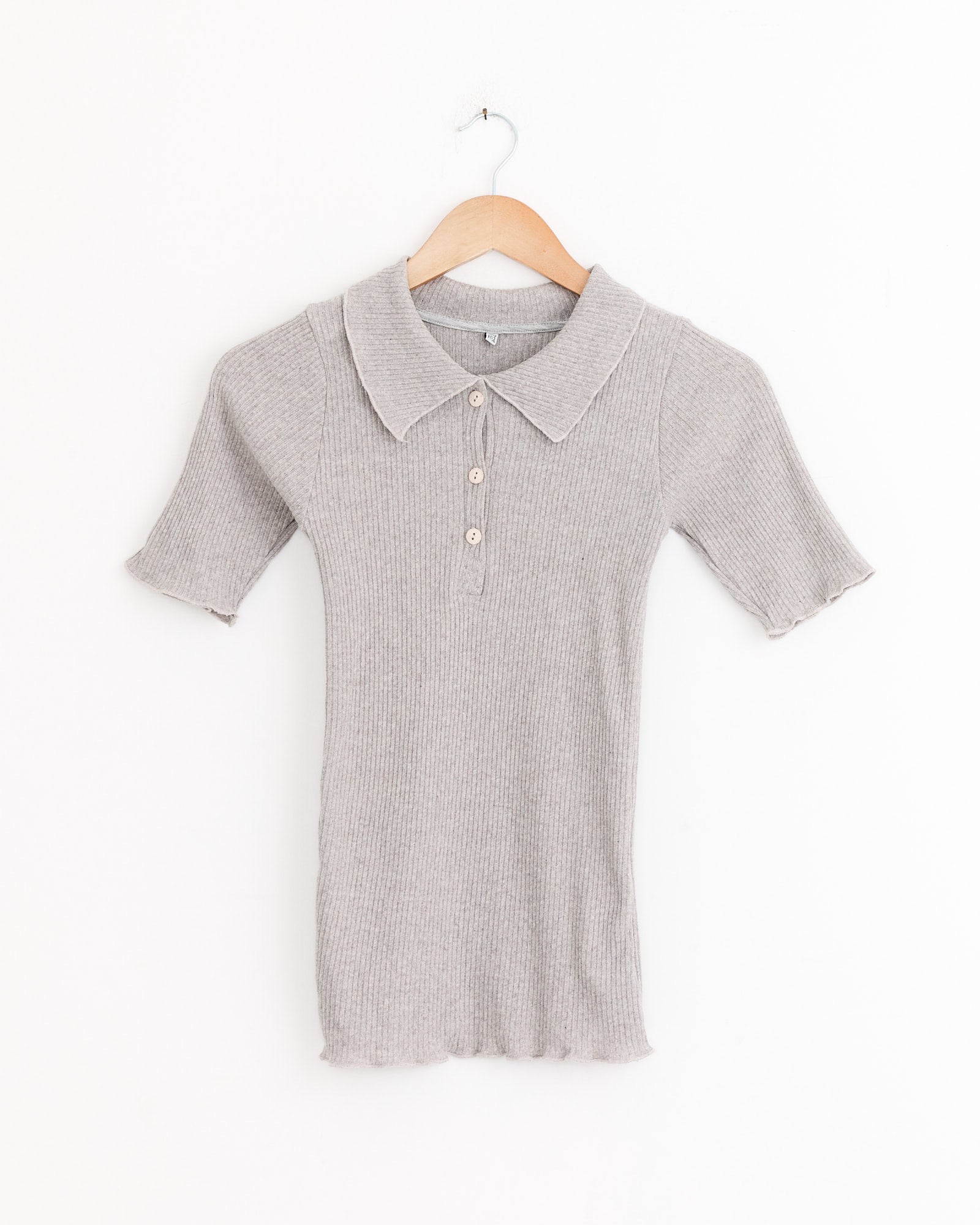 The Baserange Dual Polo in Grey Melange features a collar, three buttons, and short sleeves, shown ribbed knit on a wooden hanger against a white background.
