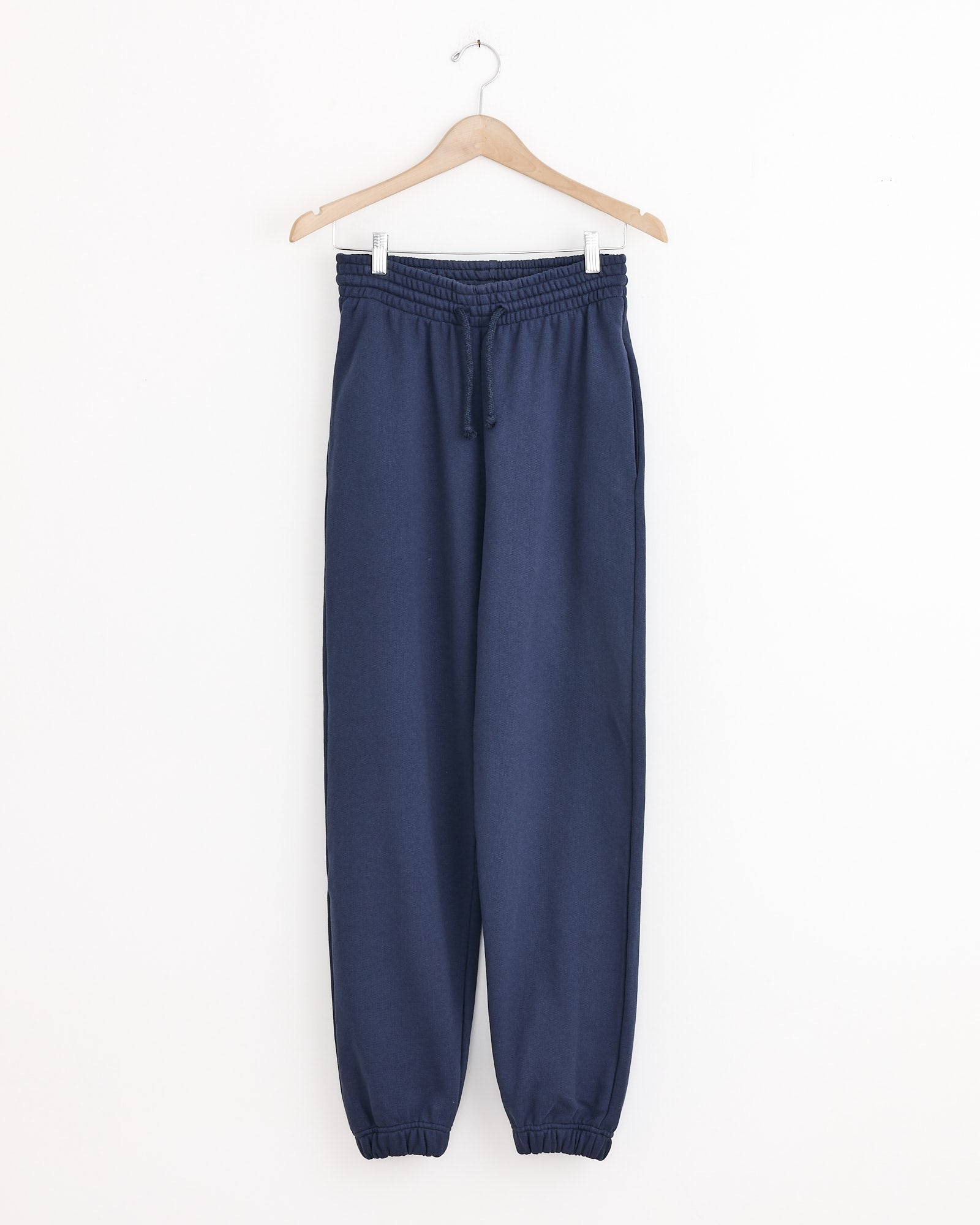 The Baserange Sweatpant in Echo Blue, made from recycled cotton with an elastic waistband, drawstring, and ankle cuffs, hangs on a wooden hanger against a white background—ideal for eco-friendly loungewear.