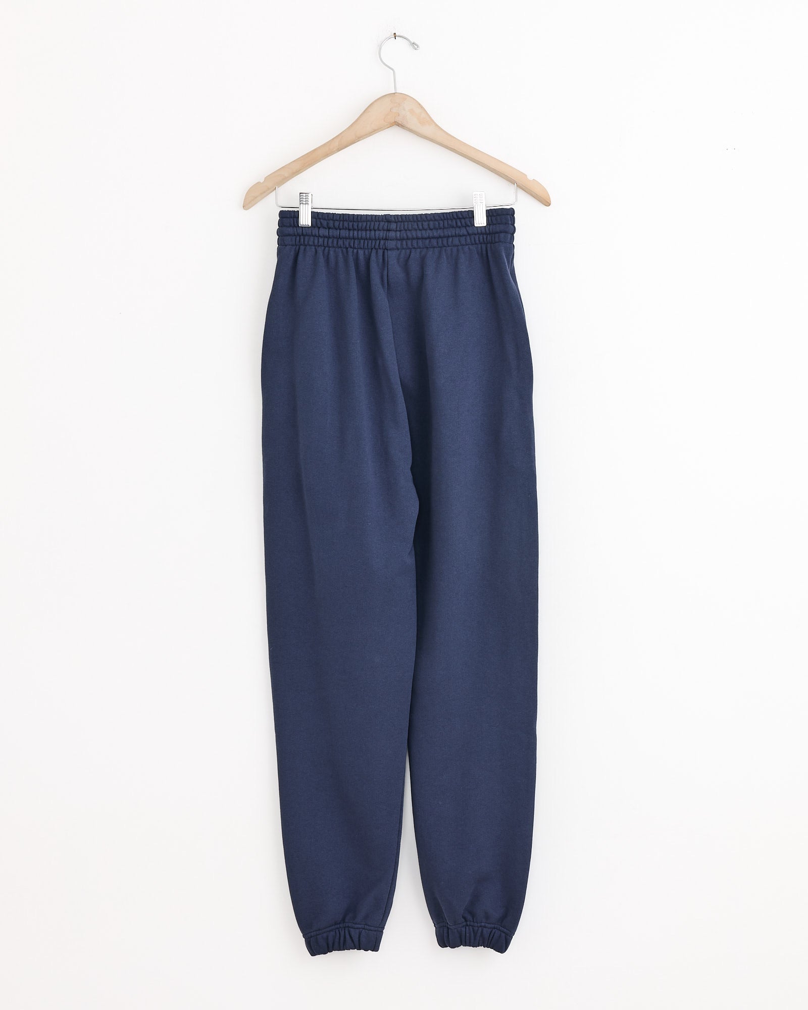 The Baserange Sweatpant in Echo Blue, crafted from recycled cotton, hangs on a wooden hanger against a white background—an ideal choice for sustainable loungewear.