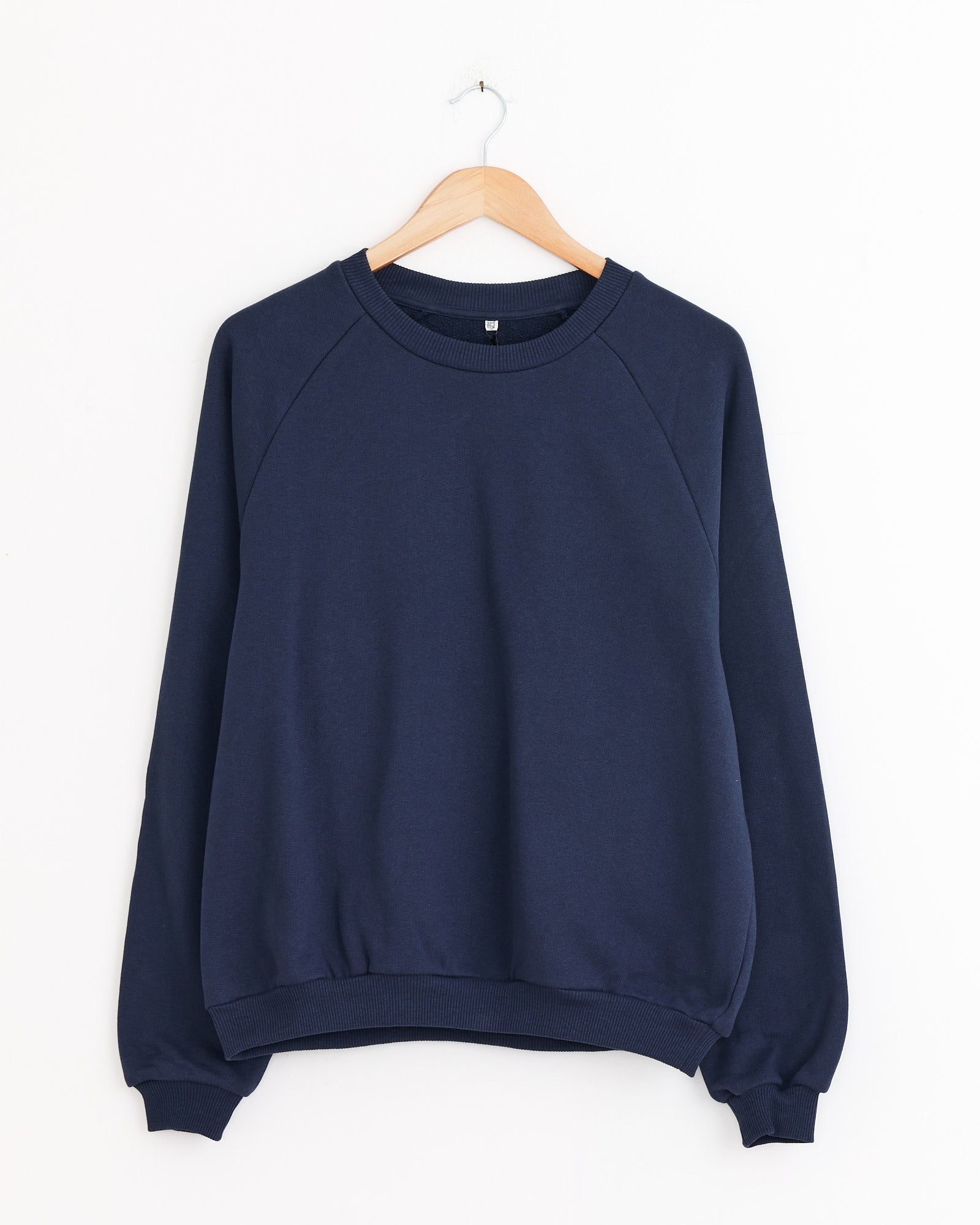 The Baserange Rim Raglan Sweatshirt in Echo Blue, made from recycled cotton, is displayed on a wooden hanger against a white background. It features long sleeves with ribbed cuffs and hem for a classic look.
