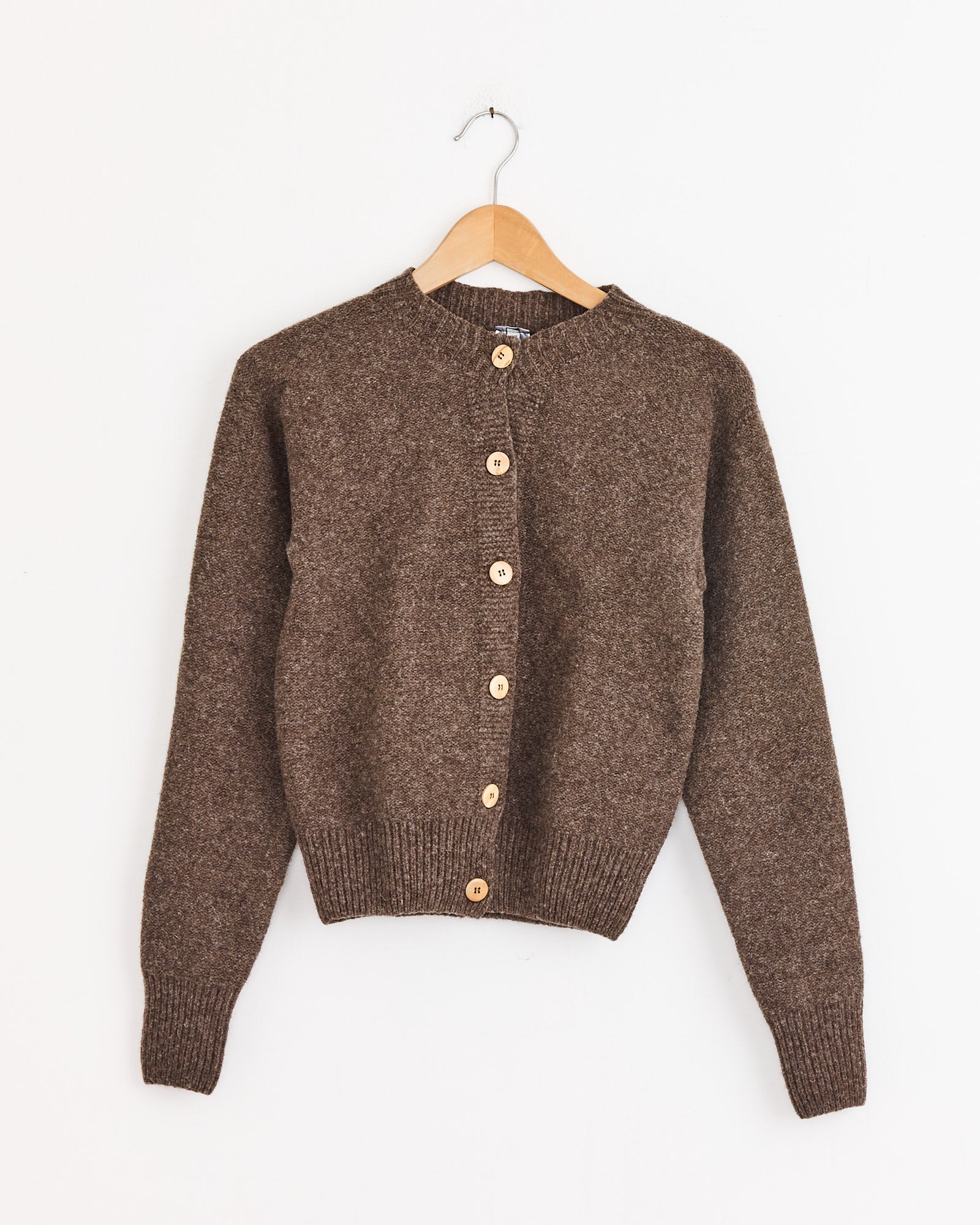 The Baserange Tier Cardigan in Burel Brown is a women's knit cardigan with long sleeves and wooden front buttons, crafted from soft Arles merino wool, displayed on a wooden hanger against a plain white background.