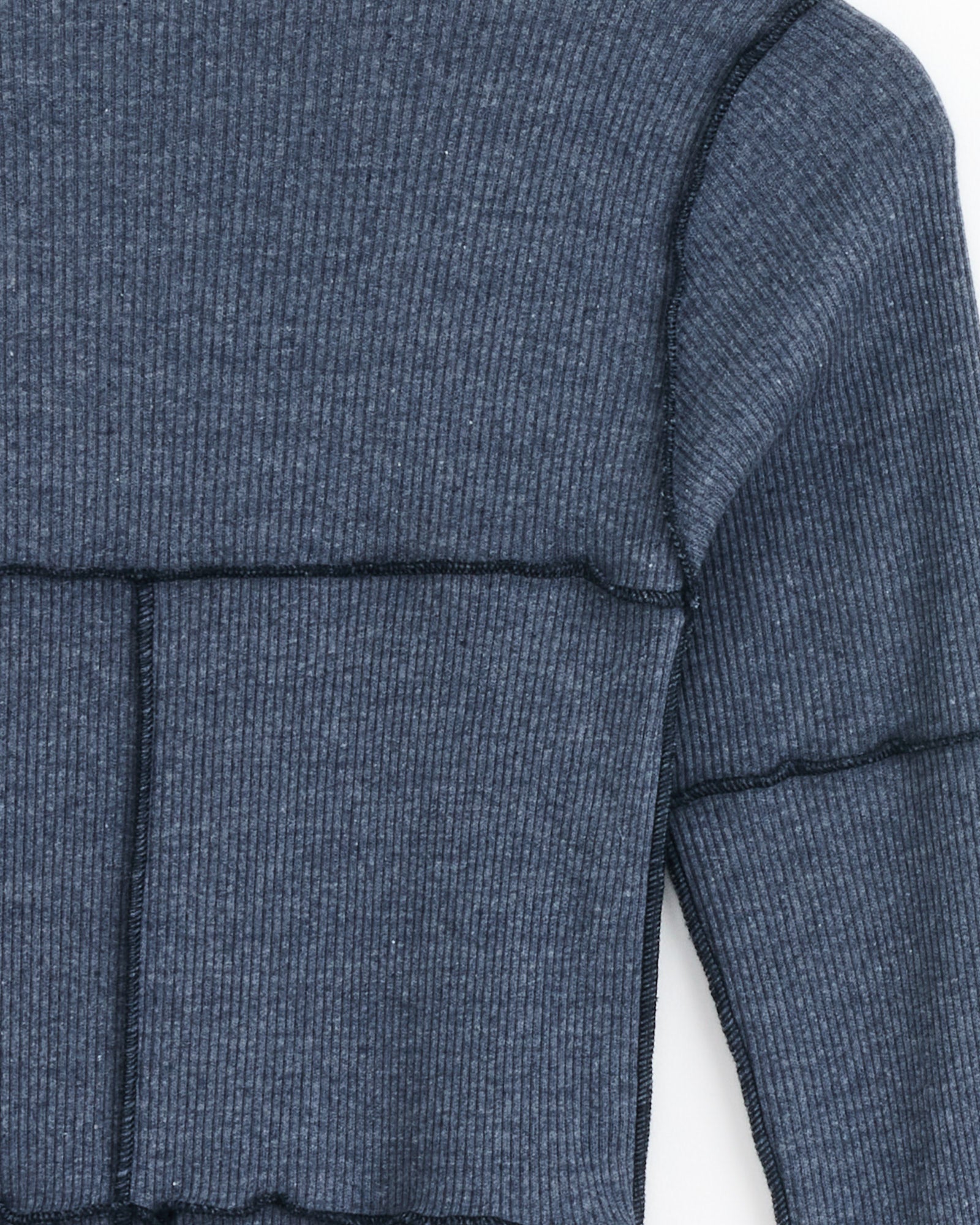 Close-up of the Baserange Cinder Tee in Dark Denim, a blue long-sleeve organic cotton ribbed top with black seam stitching and cropped hem, highlighting part of the upper body and one sleeve.