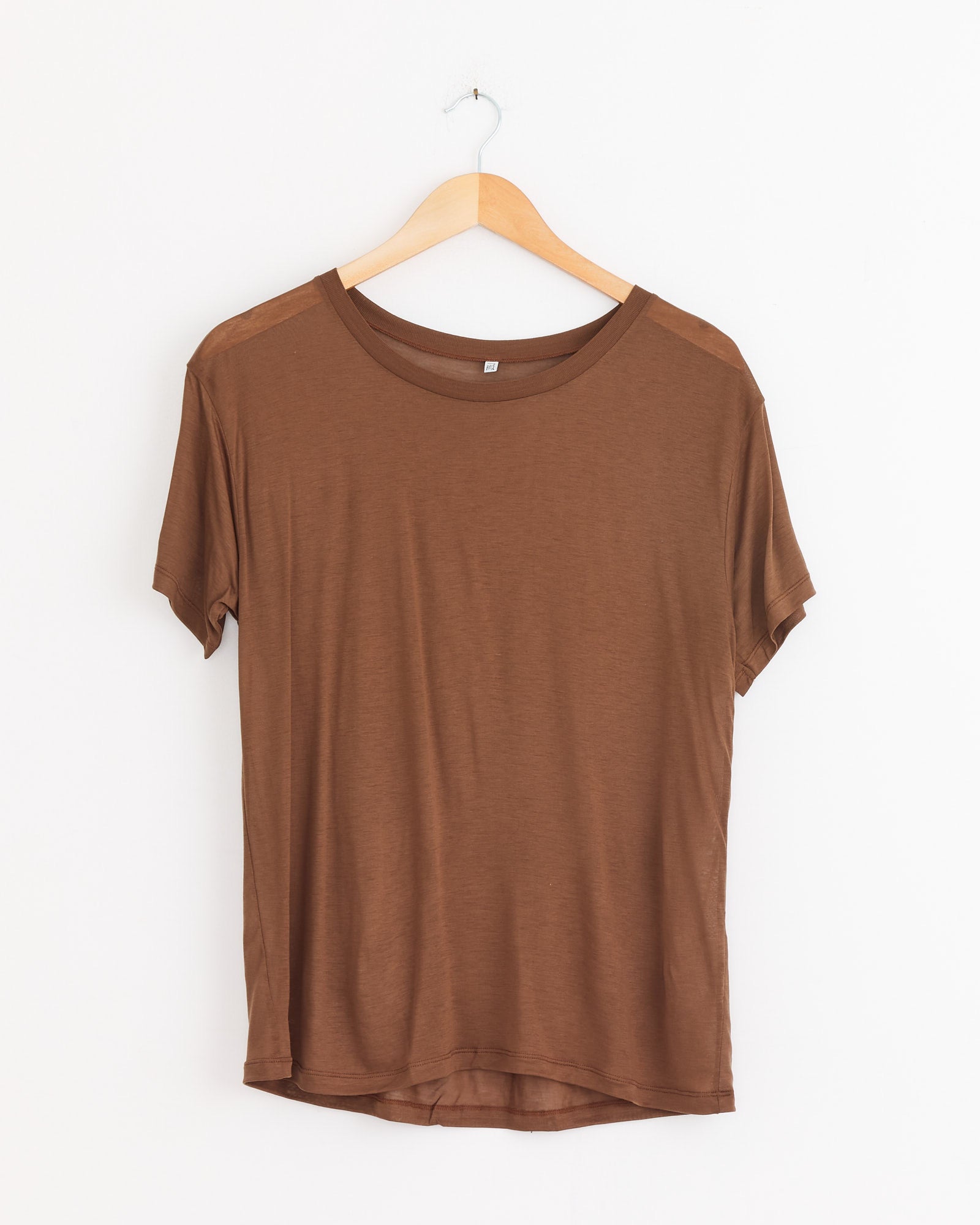 The Baserange Loose Tee in Ocular, featuring a relaxed silhouette, hangs on a wooden hanger against a white background.