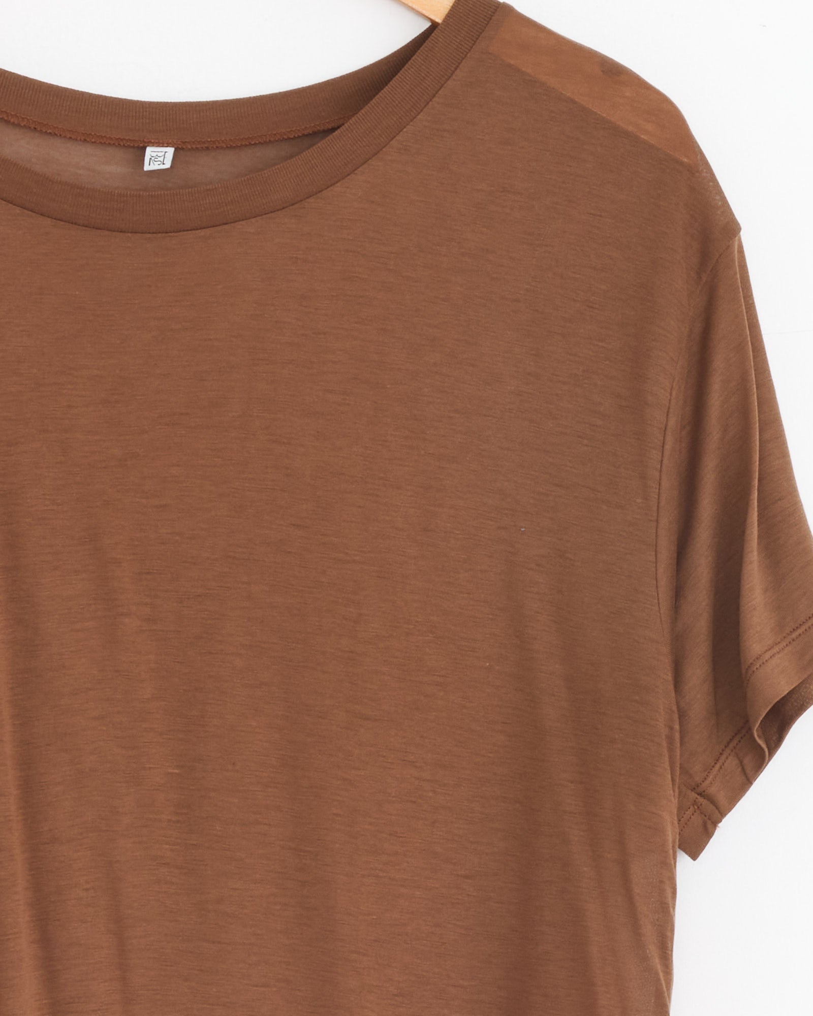 A Baserange Loose Tee in Ocular, featuring a relaxed silhouette, hangs on a wooden hanger against a white background. Only the upper half of this bamboo lyocell short-sleeve t-shirt is shown.