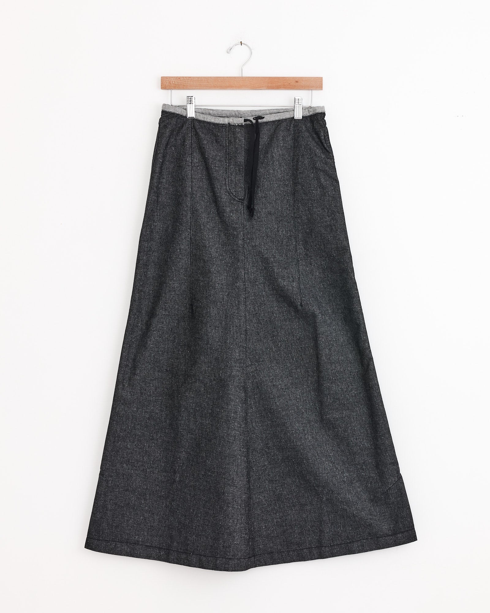 The Arthur Skirt in Black by Baserange is a long, dark gray A-line recycled denim skirt with a light gray elastic waistband and black drawstring, shown on a wooden hanger against a white background.