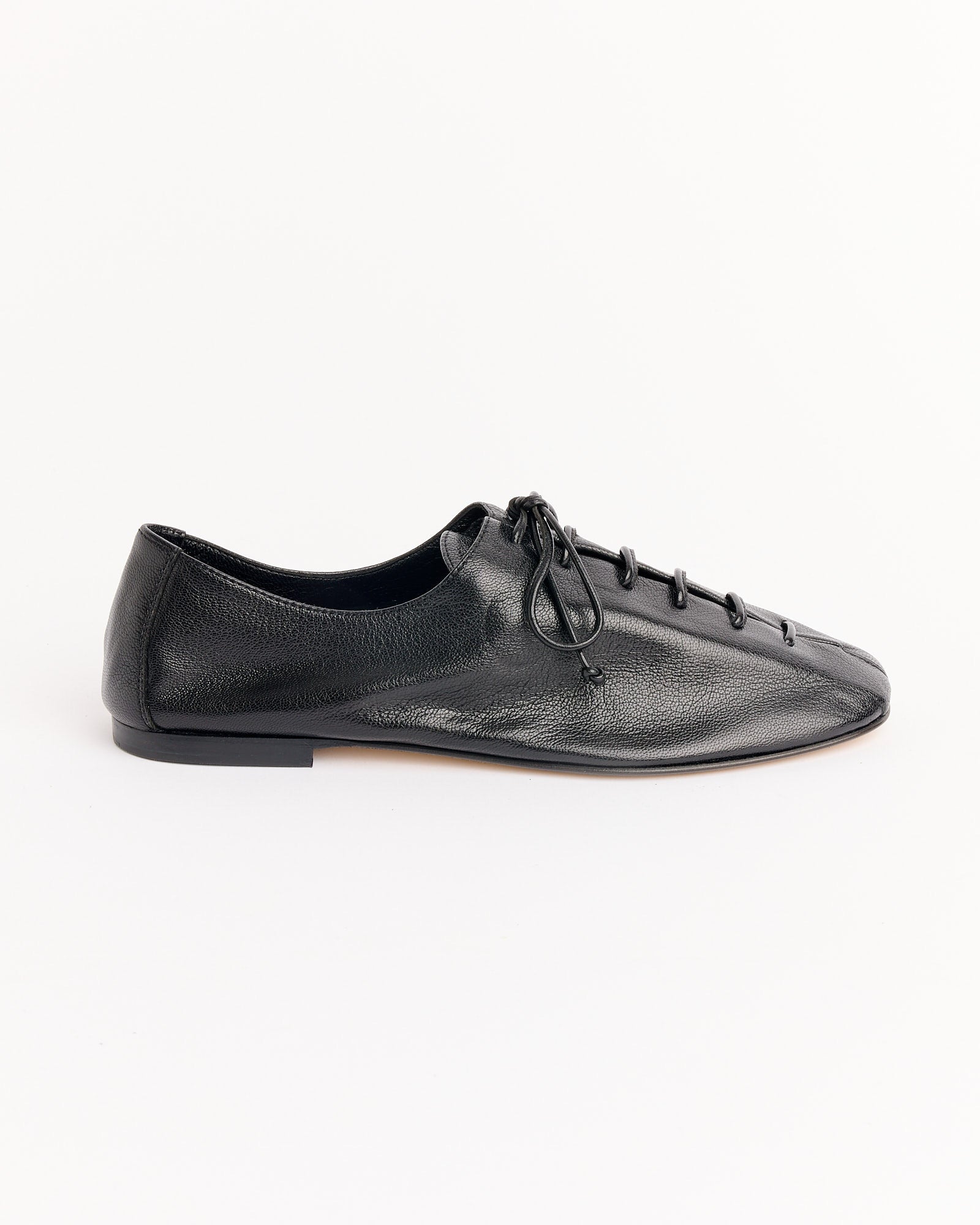The Hereu Plegada Supple Shiny Shoes in Black are black leather lace-up flats with a rounded toe and low heel, shown in side profile on a white background. Online chat is available for fit and sizing questions.