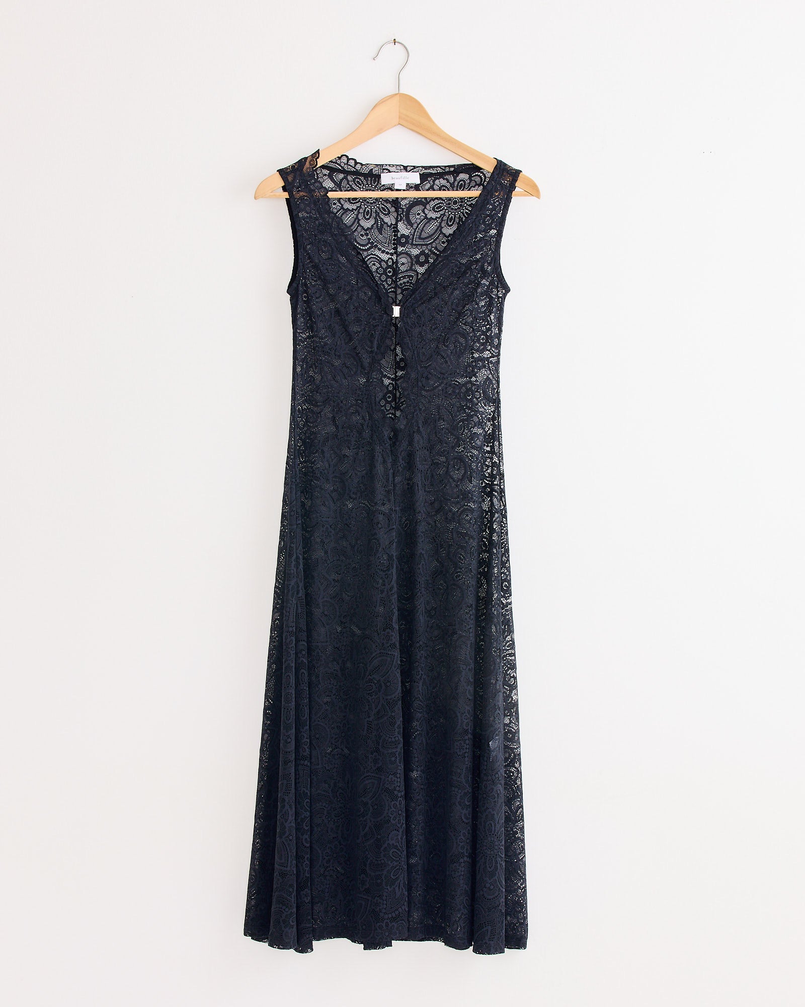 The Beaufille Twain Lace Dress in Black, a sleeveless slim-fit style with a V-neckline, hangs on a wooden hanger against a plain white wall.