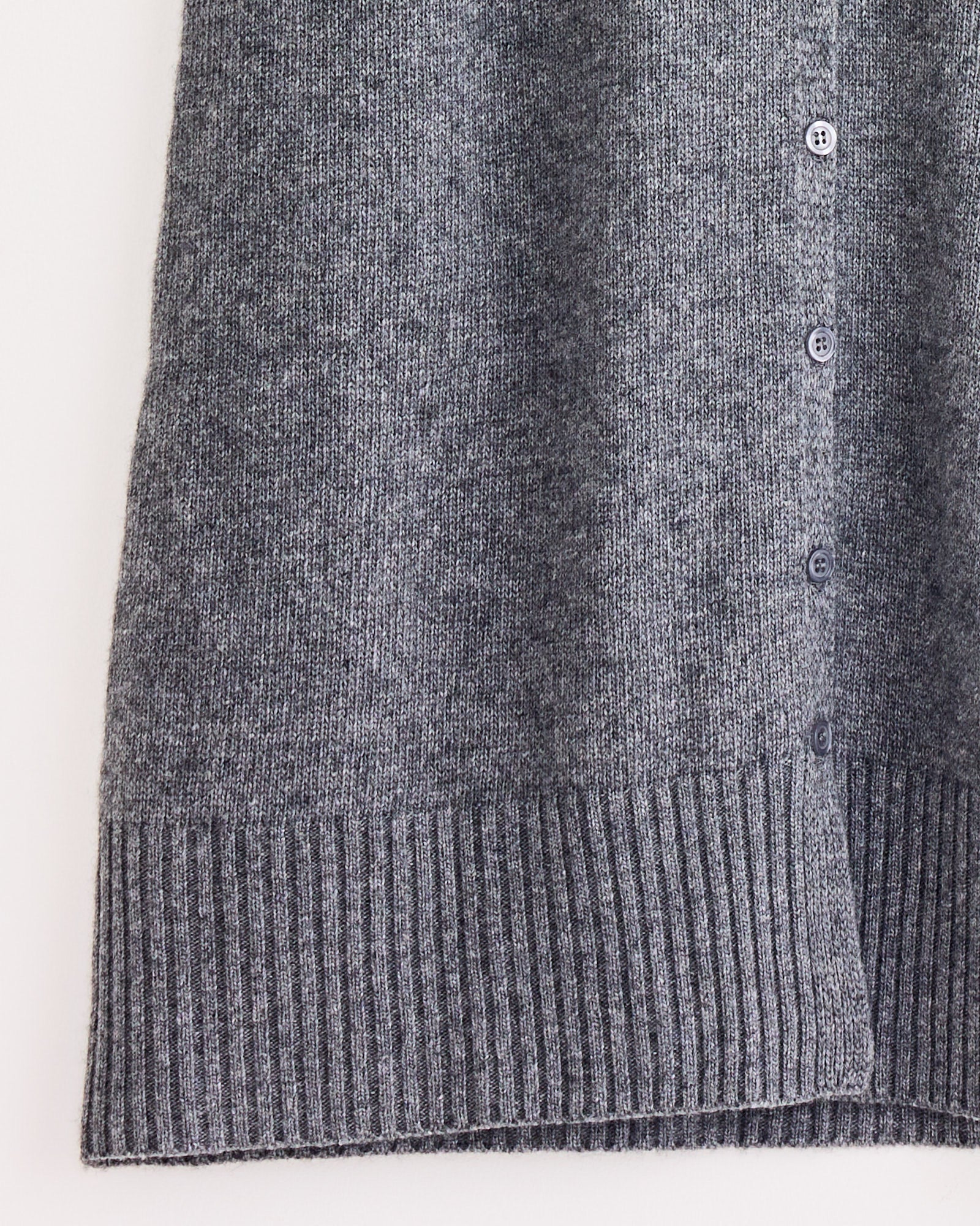Close-up of Beaufille’s Amina Skirt in Light Grey, styled with a gray cardigan featuring a ribbed hem and small front buttons, set against a plain white background.