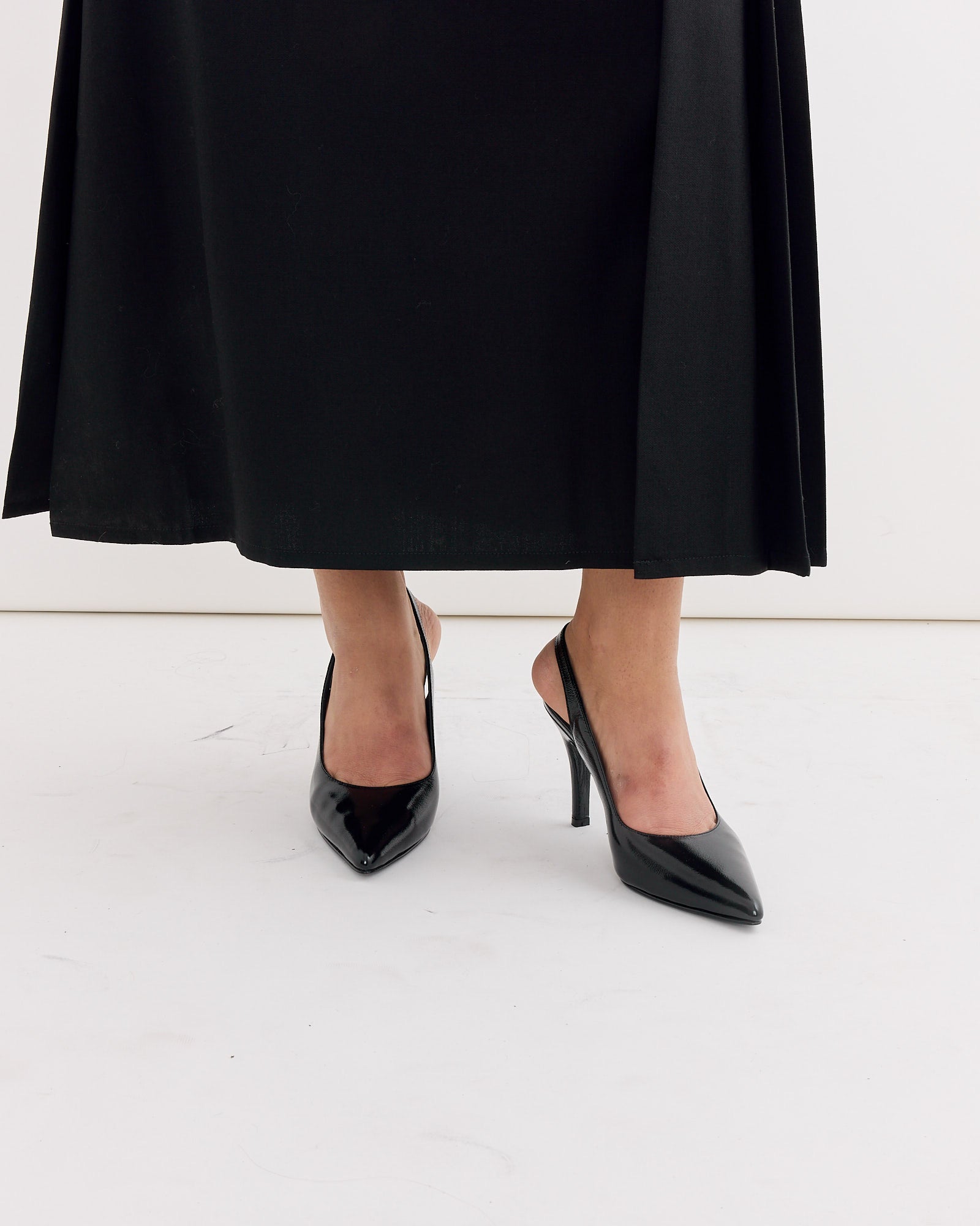 A person wearing a long black skirt and Rachel Comey’s Cheke Sling Back Heel in Black stands on a white floor against a white background.
