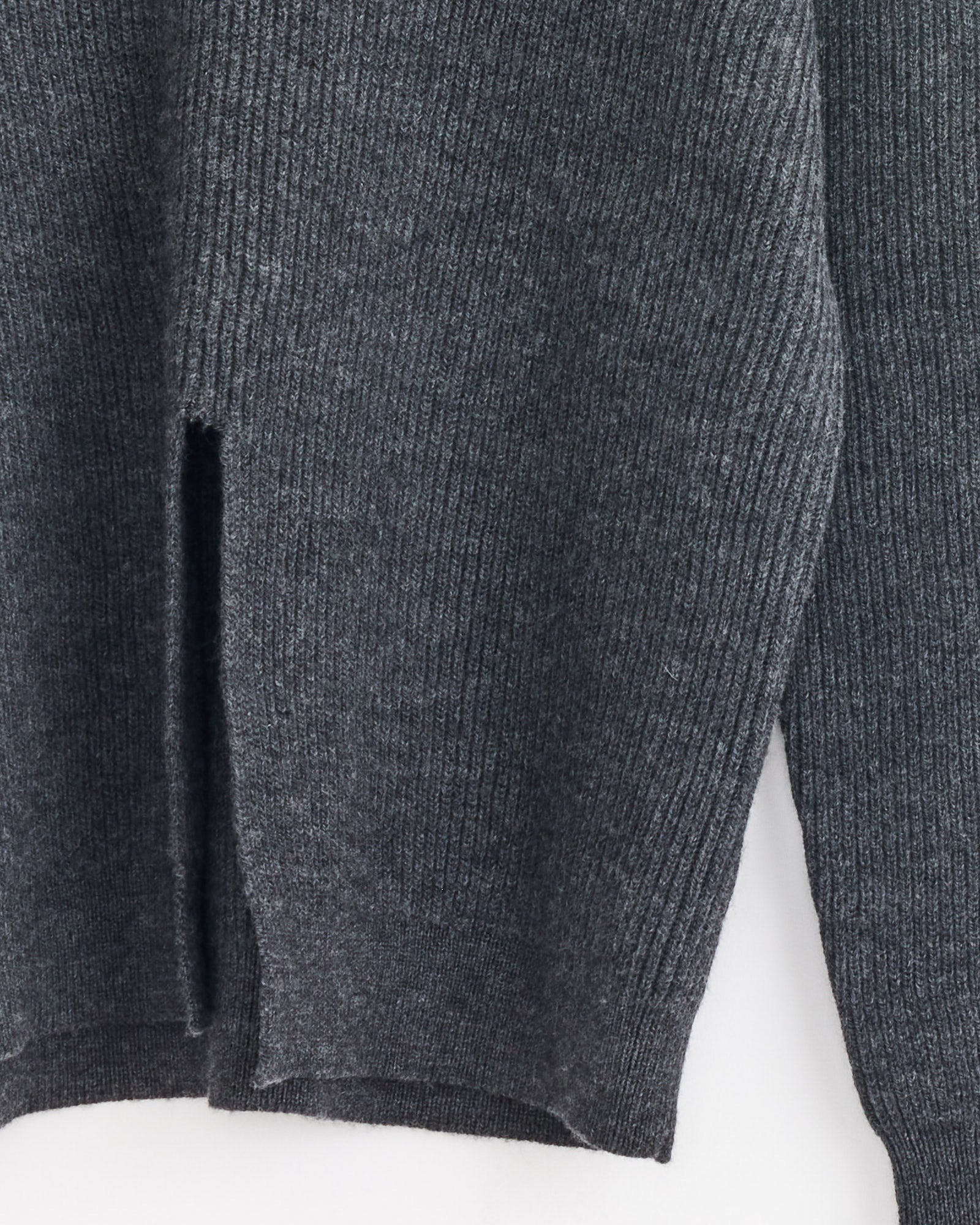 A close-up of Tibi's Split Front Easy Pullover in Dark Heather Grey shows its ribbed wool knit texture, modern silhouette, and vertical slit detail near the hem.