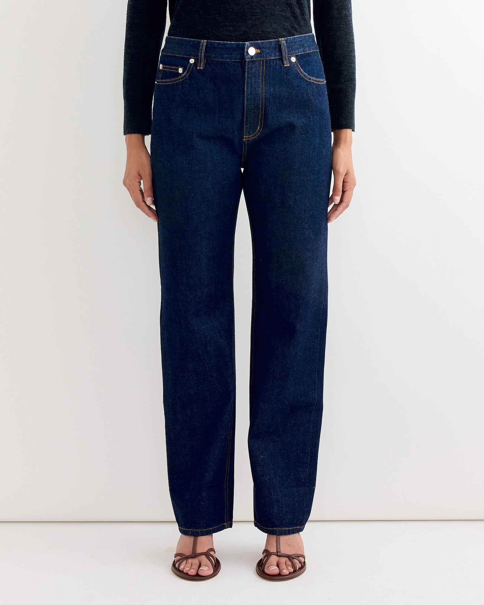 A person models Tibis 5 Pocket Alec Jean in Dark Denim, paired with a black long-sleeve shirt and brown sandals, standing against a white background. The photo is cropped at the shoulders.