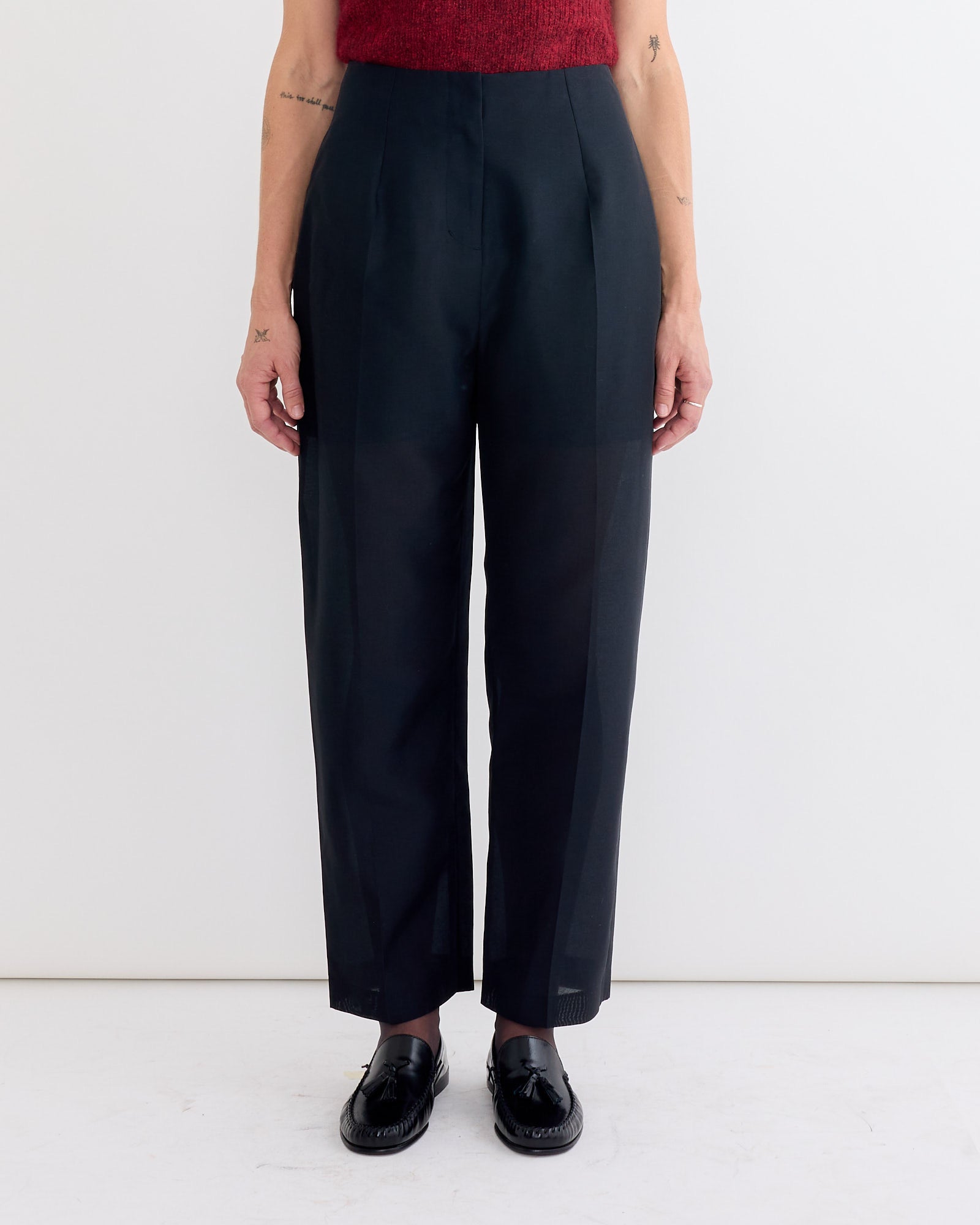 A person wearing Amomento's Organza Structure Pant in Black, a sleeveless red top, and black loafers stands against a plain white background with arms relaxed at their sides.