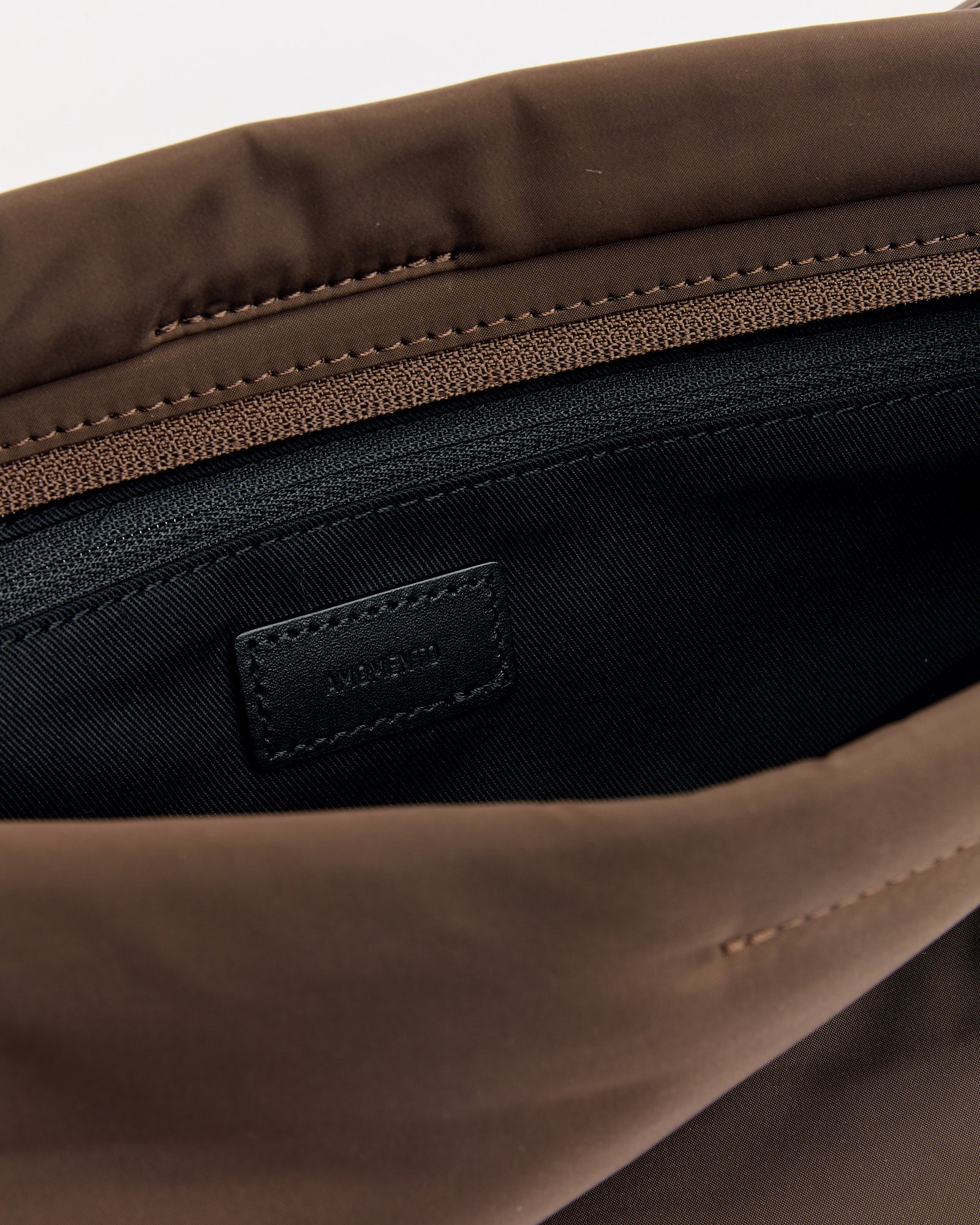 Close-up of the Small Padded Bag in brown by Amomento, opened to reveal the black interior lining and a small black fabric label sewn inside.