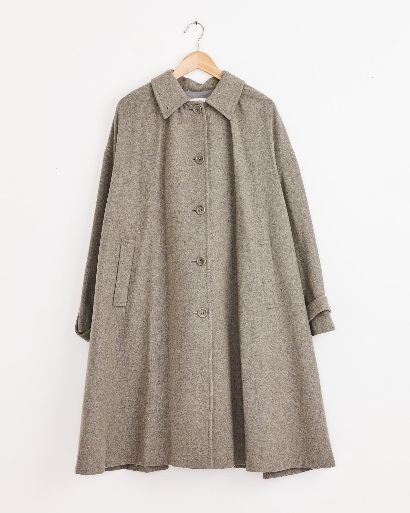 The Amomento Shirring Coat in Grey Blue features a wide flare silhouette, large collar, button-down front, long sleeves, and two side pockets, shown hanging on a wooden hanger against a plain white background.