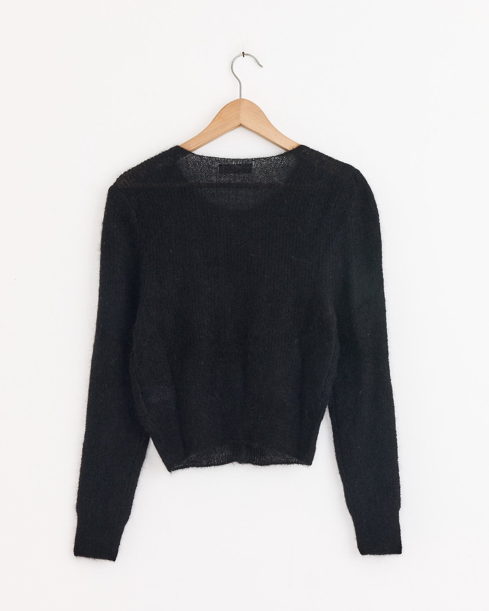 The Amomento Round Neck Sheet Cardigan in Black, with long sleeves and a mohair blend, is displayed on a wooden hanger against a plain white wall.