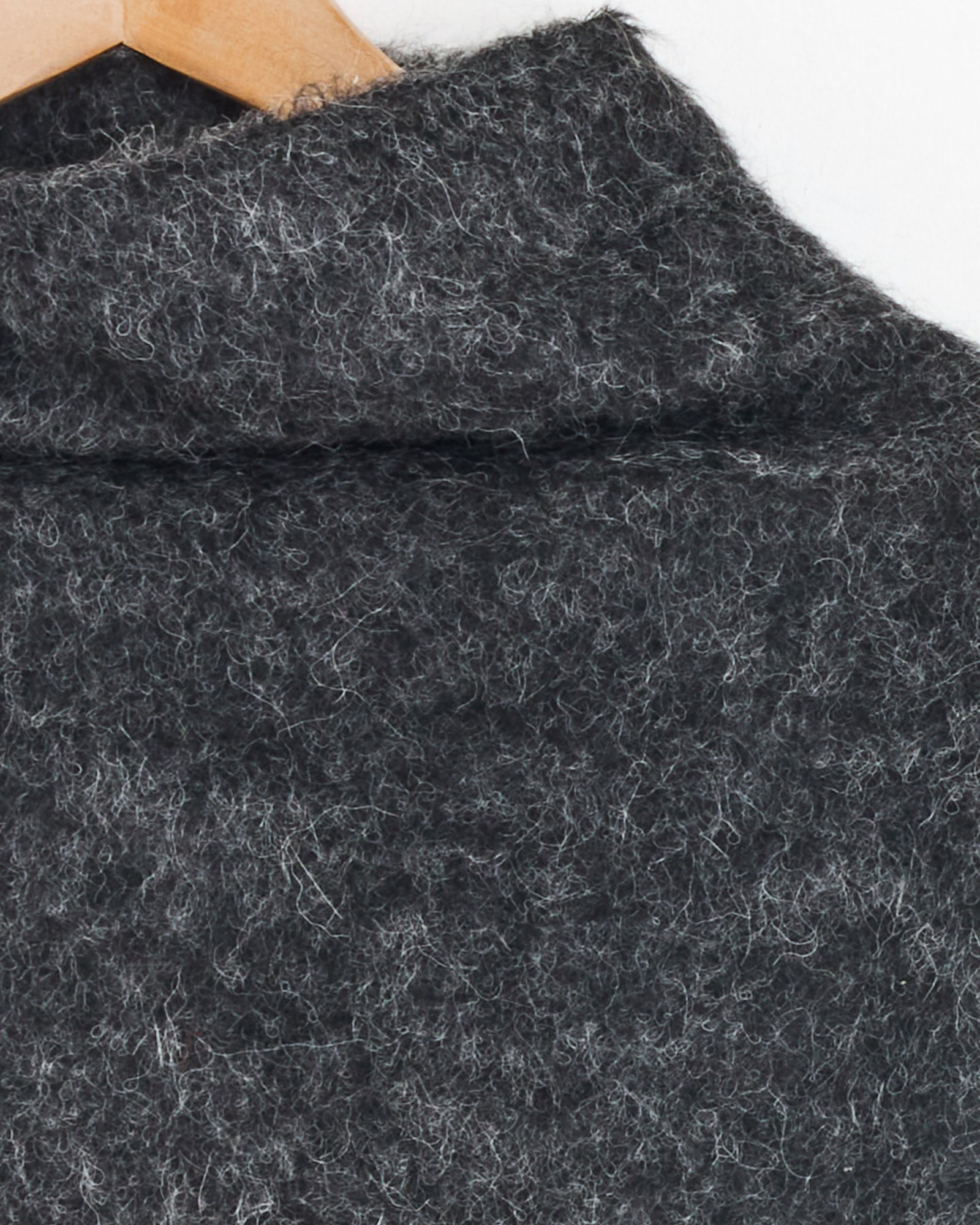 Close-up of the Amomento Alpaca Top in Charcoal on a wooden hanger, showcasing its textured fabric, collar detail, and adjustable hem.