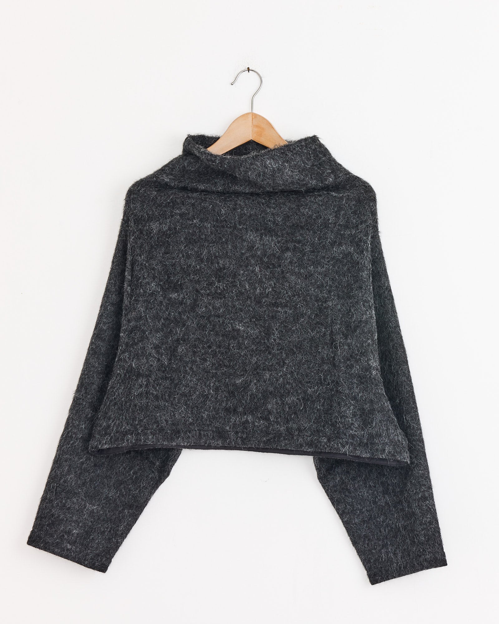 The Amomento Alpaca Top in Charcoal, featuring long sleeves, a high neck, fuzzy texture, and an adjustable hem, is shown on a wooden hanger against a plain white background.
