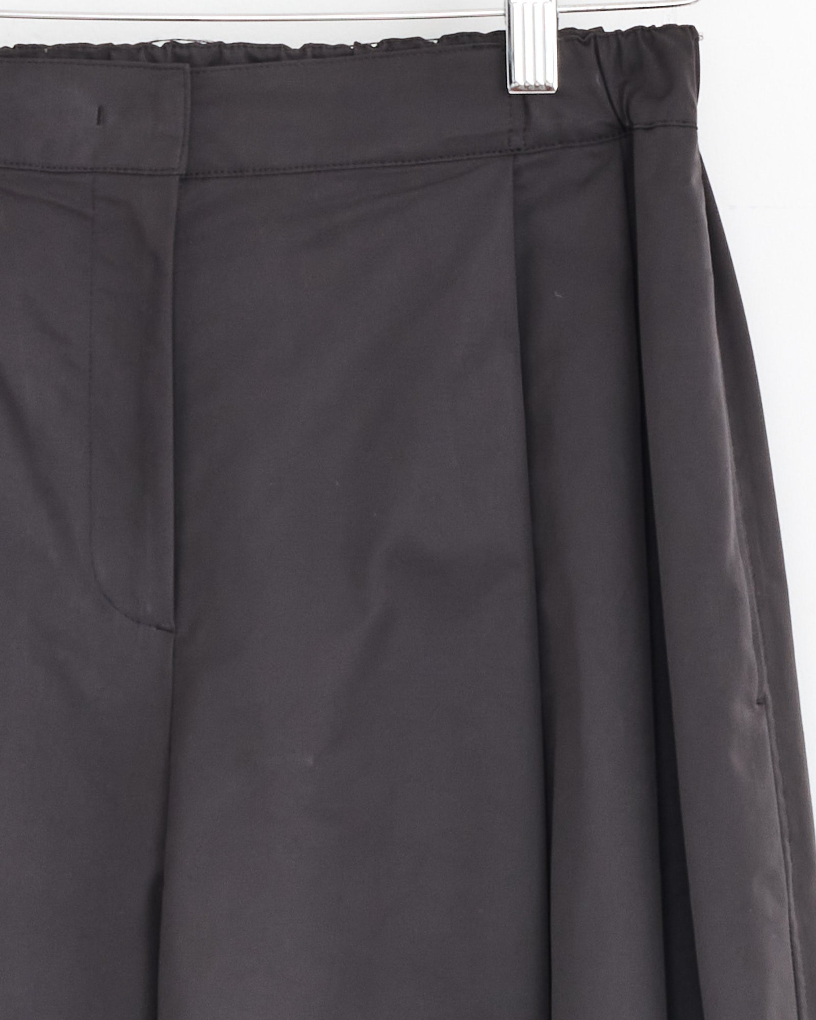 Close-up of the upper section of Amomento's Two Tuck Balloon Pant in Charcoal on a hanger, focusing on the waistband, pleats, and part of the zipper area.