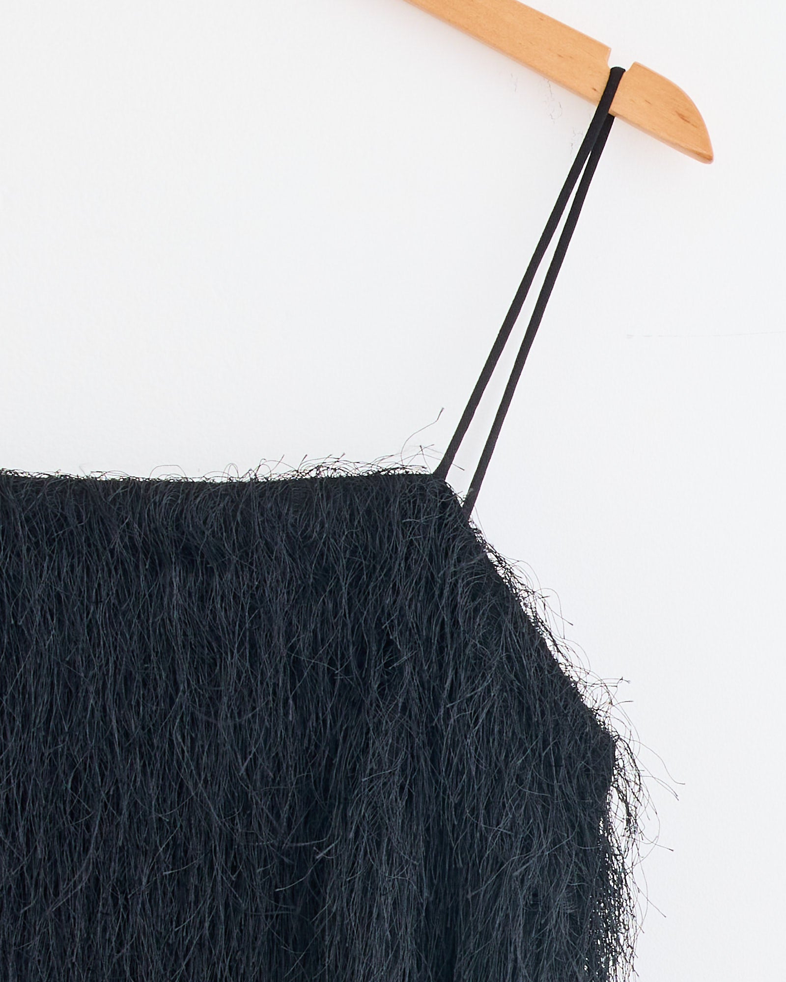 Close-up of the Ledo Dress in Black by By Malene Birger, featuring a textured, fuzzy finish and thin double straps, hanging on a wooden hanger against a white background—perfect for chic eveningwear.