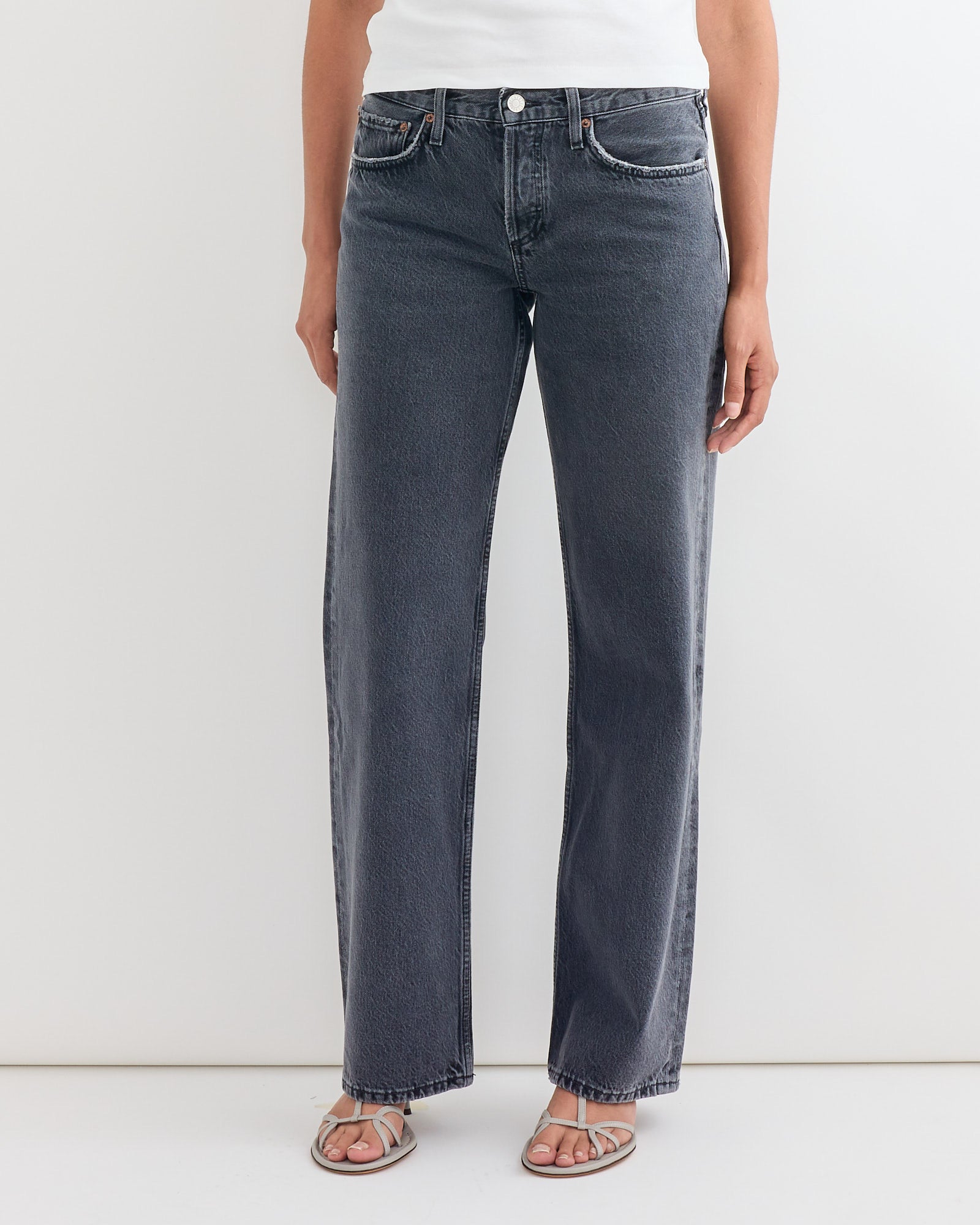 A person wears a white top, AGOLDE’s Low Rise Loose Jean in Symbolic, and light sandals while standing against a plain white background—ideal for viewing fit or referencing sizing details in an online chat.