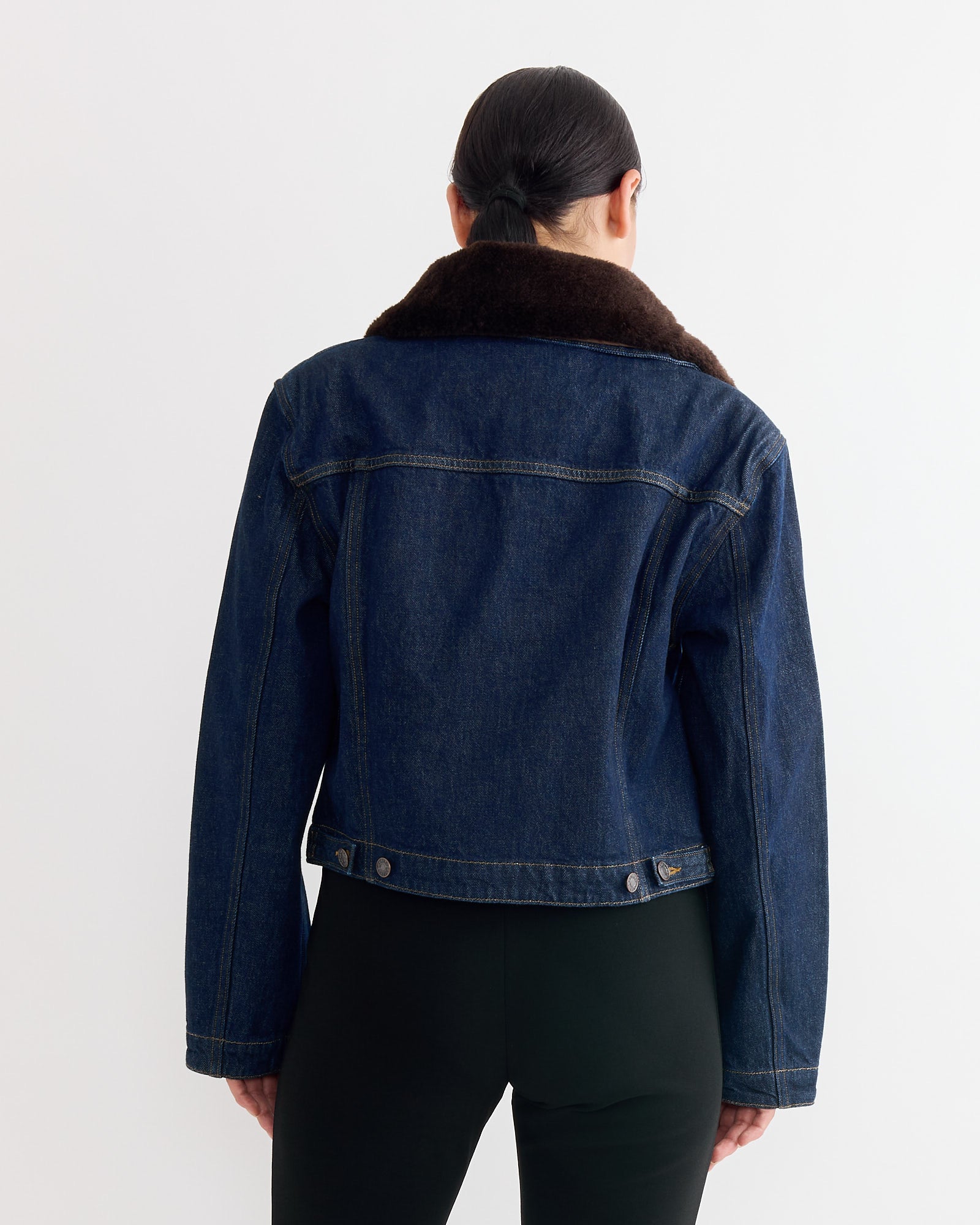 A person with dark hair pulled back wears the AGOLDE Walker Jacket in Rinse, a cropped denim style with a brown faux fur collar, shown from the back against a plain white background.