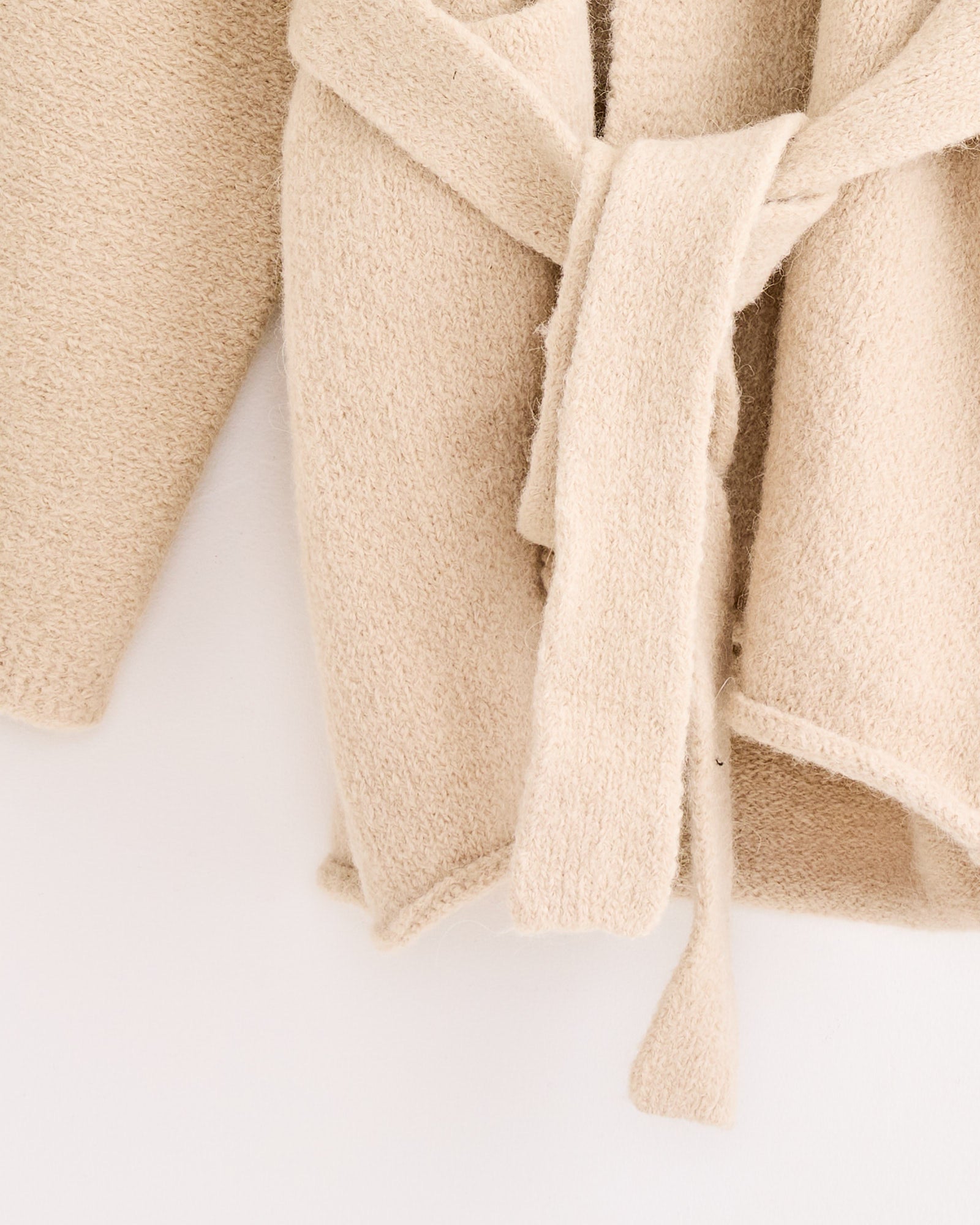 Close-up of the Lauren Manoogian Coto Cardigan, a beige, textured hand-loomed alpaca-blend knit with a matching fabric belt at the waist, shown against a plain white background.