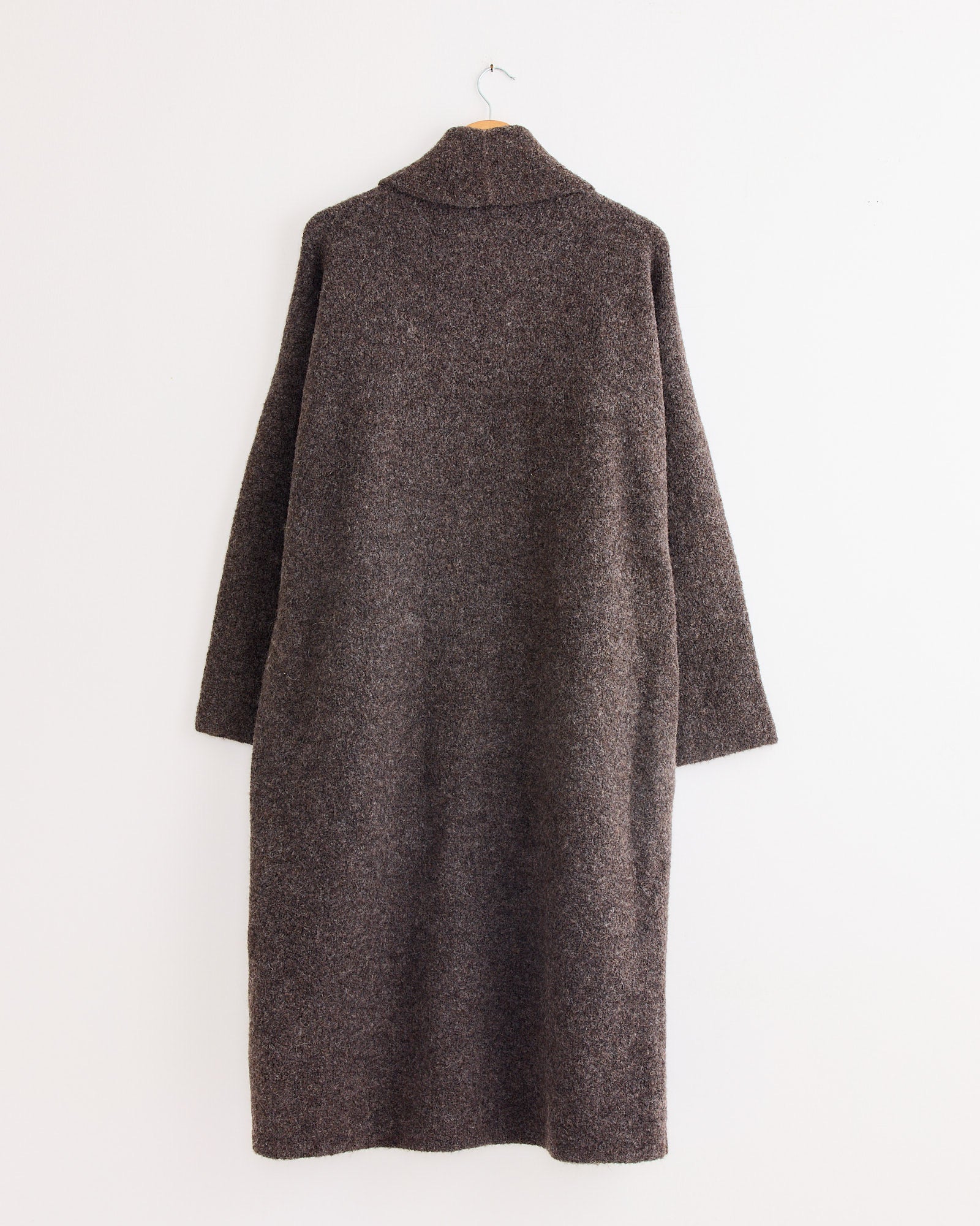 The Lauren Manoogian Double Face Long Coat in Blackened, made with a soft woolen texture and relaxed fit, hangs on a hanger against a plain white wall.