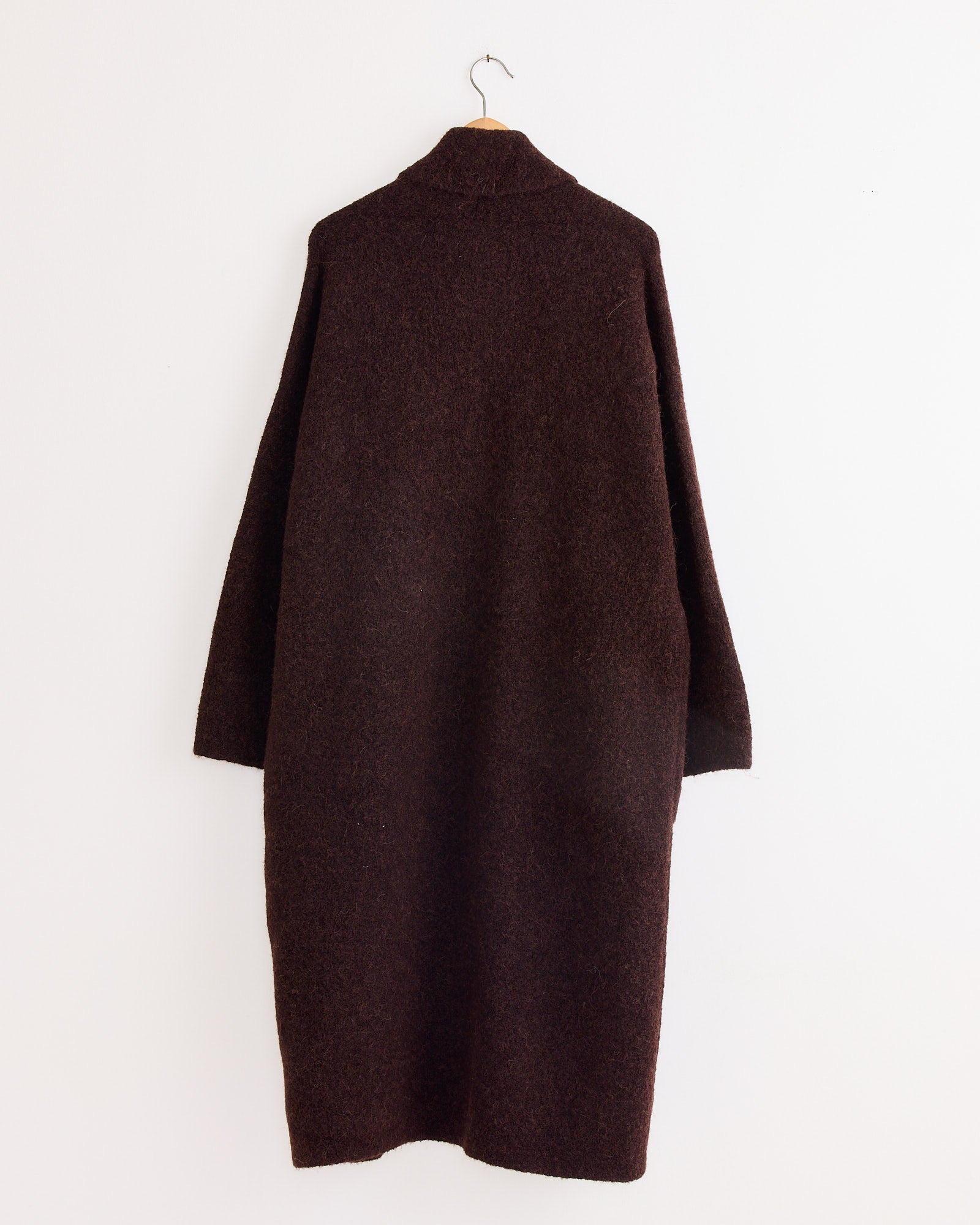 A Lauren Manoogian Double Face Long Coat in Merlot, featuring long sleeves, is shown from the back on a wooden hanger against a plain white wall.