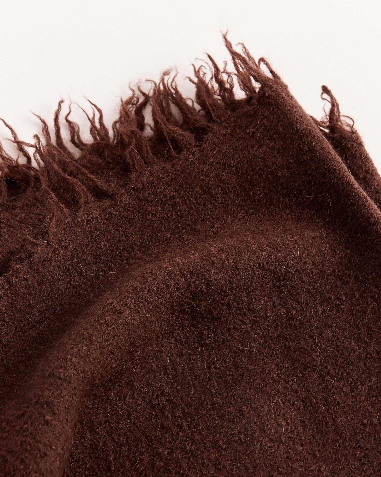 A close-up of a soft, textured brown fabric with a frayed edge, resembling the Lauren Manoogian Felt Fringe Scarf, spread out on a light-colored surface.